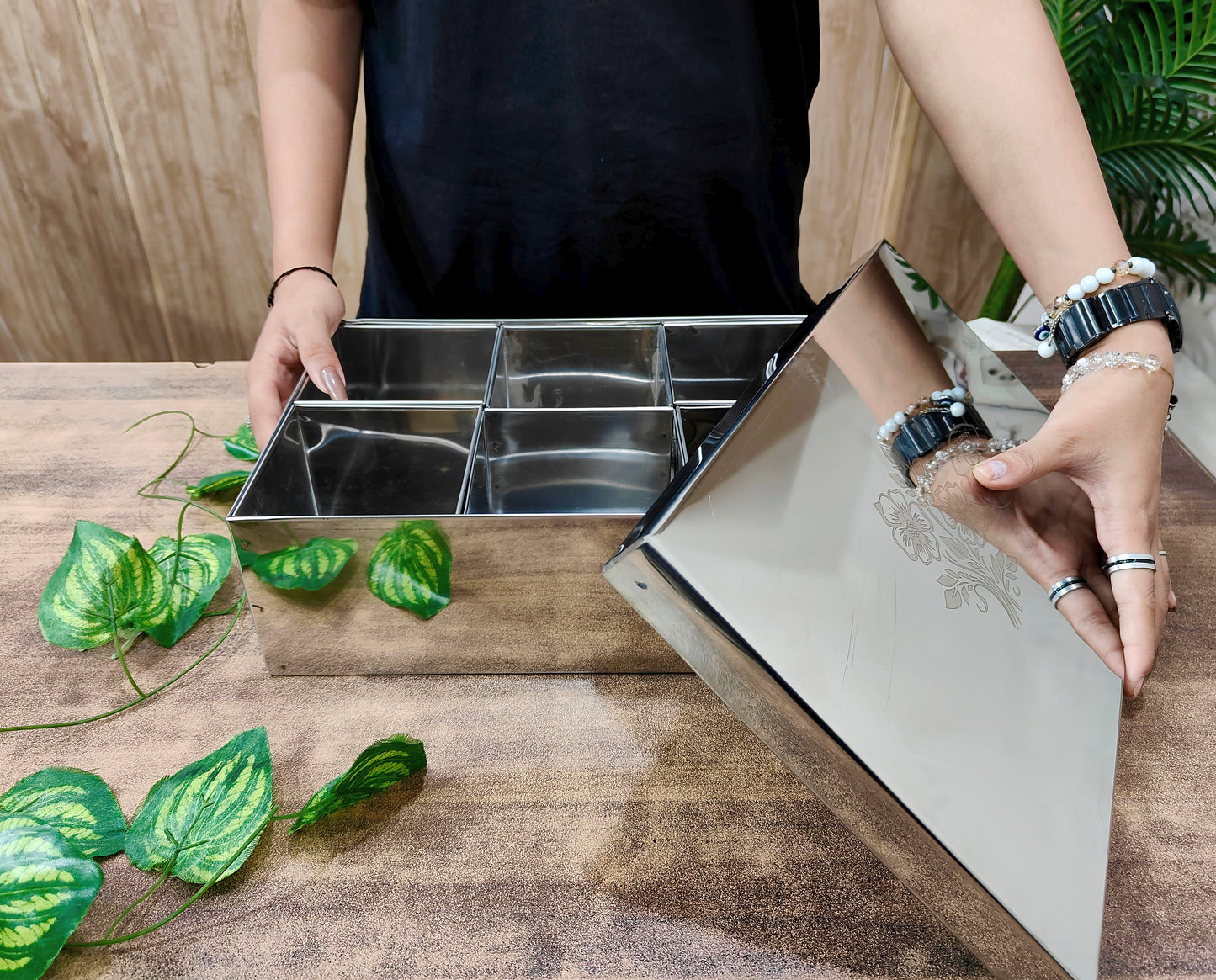 Person opening a stainless steel kitchen drawer with compartments on a wooden surface.