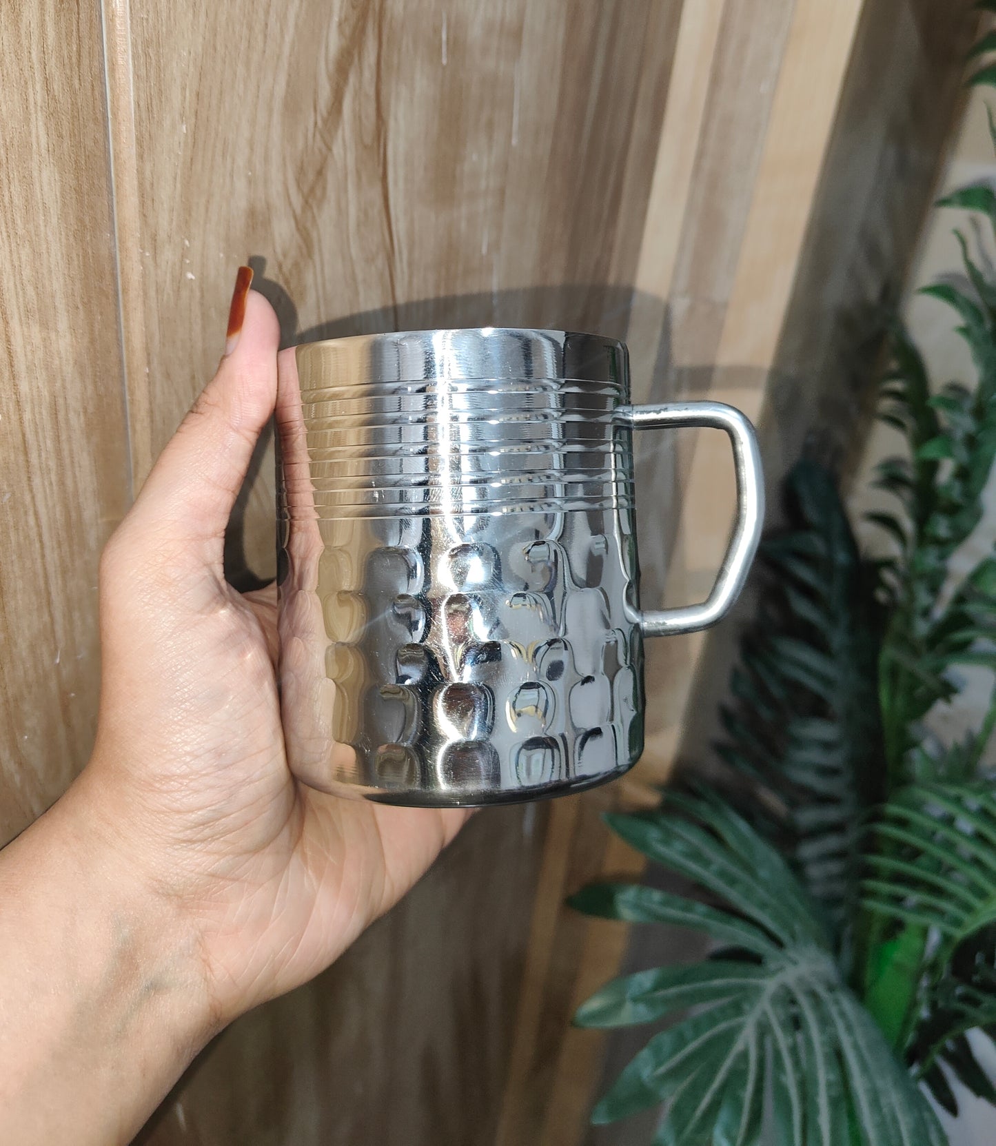 Hand holding a silver textured mug against a wooden background