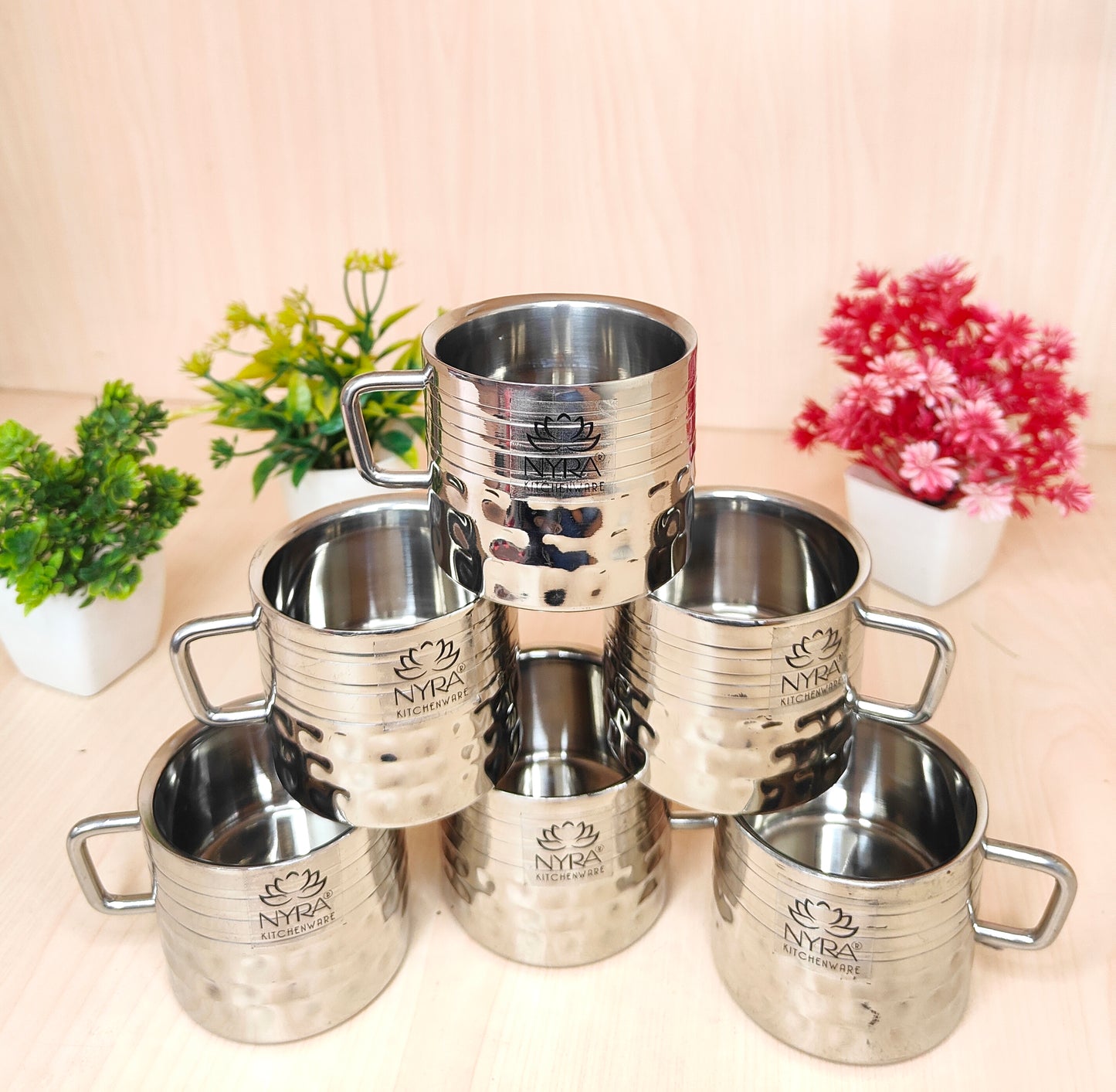 Set of silver Nyra mugs on a light surface with plants in the background