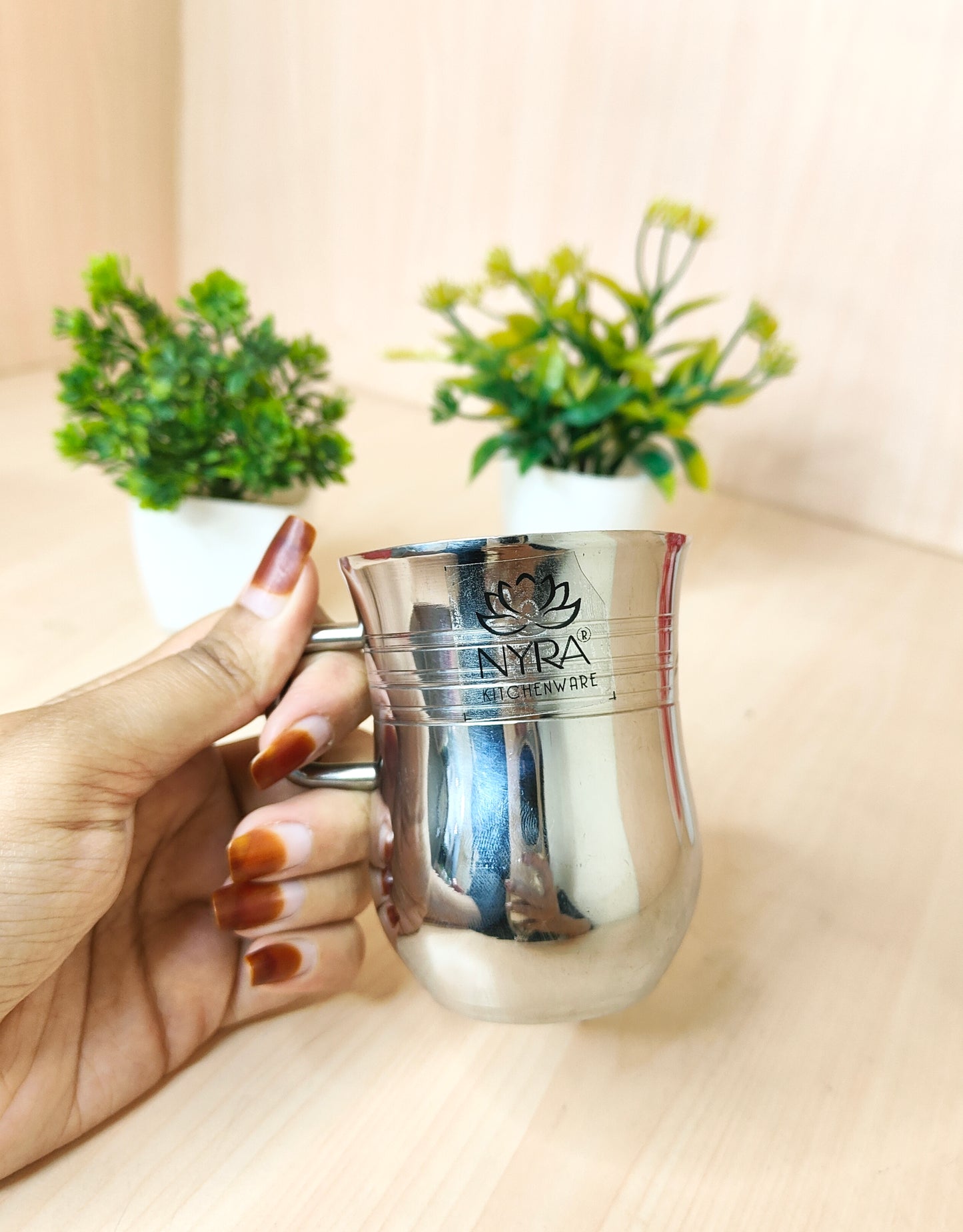 Silver cup with 'NYRA' branding held by a hand, with plants in the background.