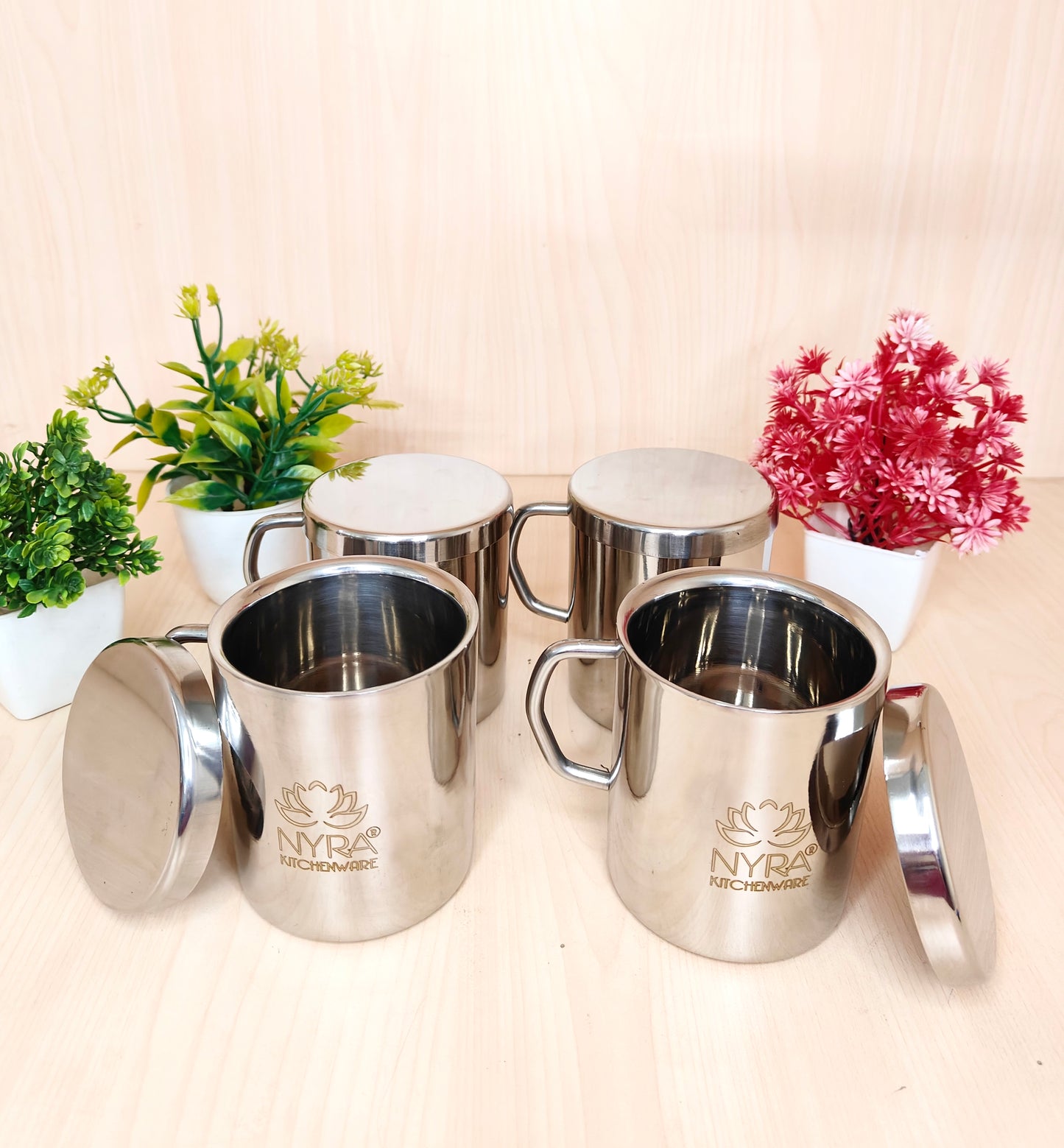 Set of silver mugs with lids on a light background, featuring the Nyra Kitchenware logo.