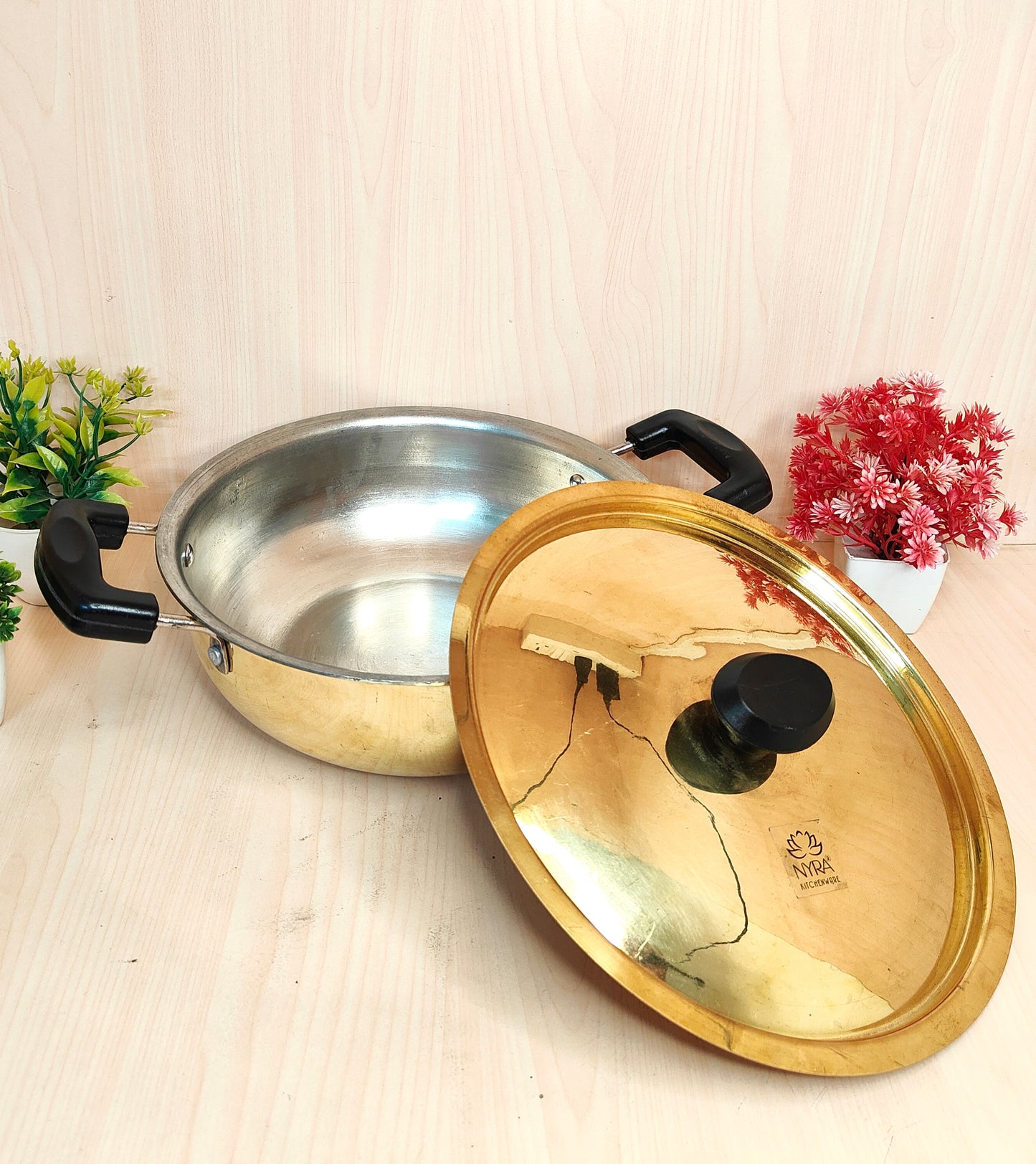 Stainless steel pot with a gold lid on a light wooden surface.