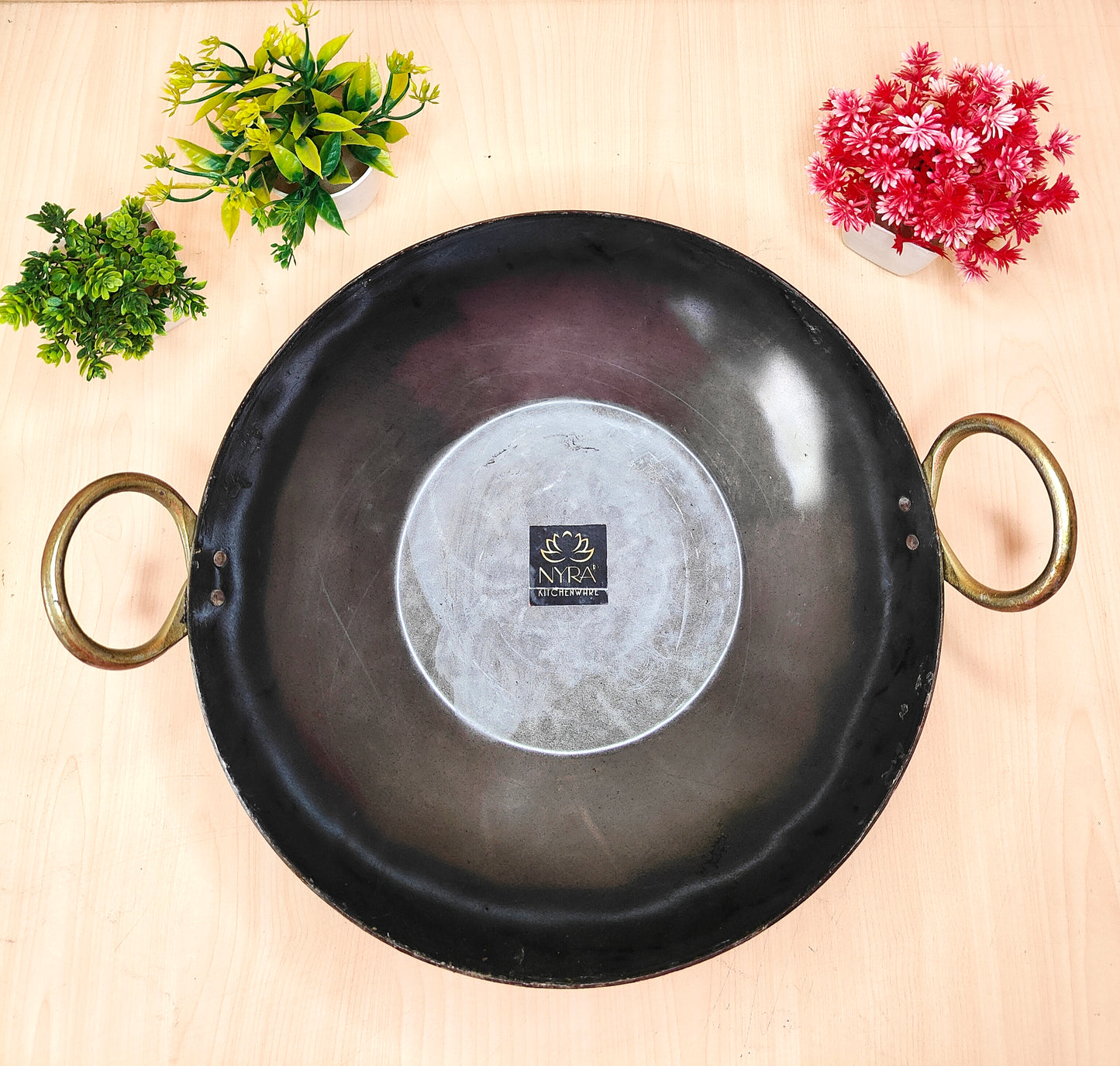Black frying pan with handles on a light wooden surface with decorative plants.