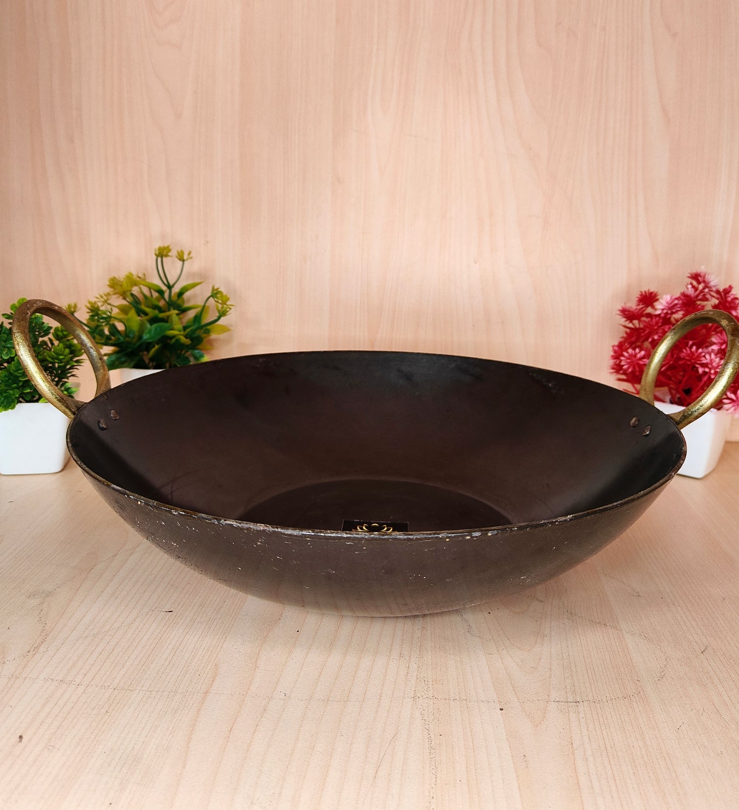 Black wok with gold handles on a light wooden surface