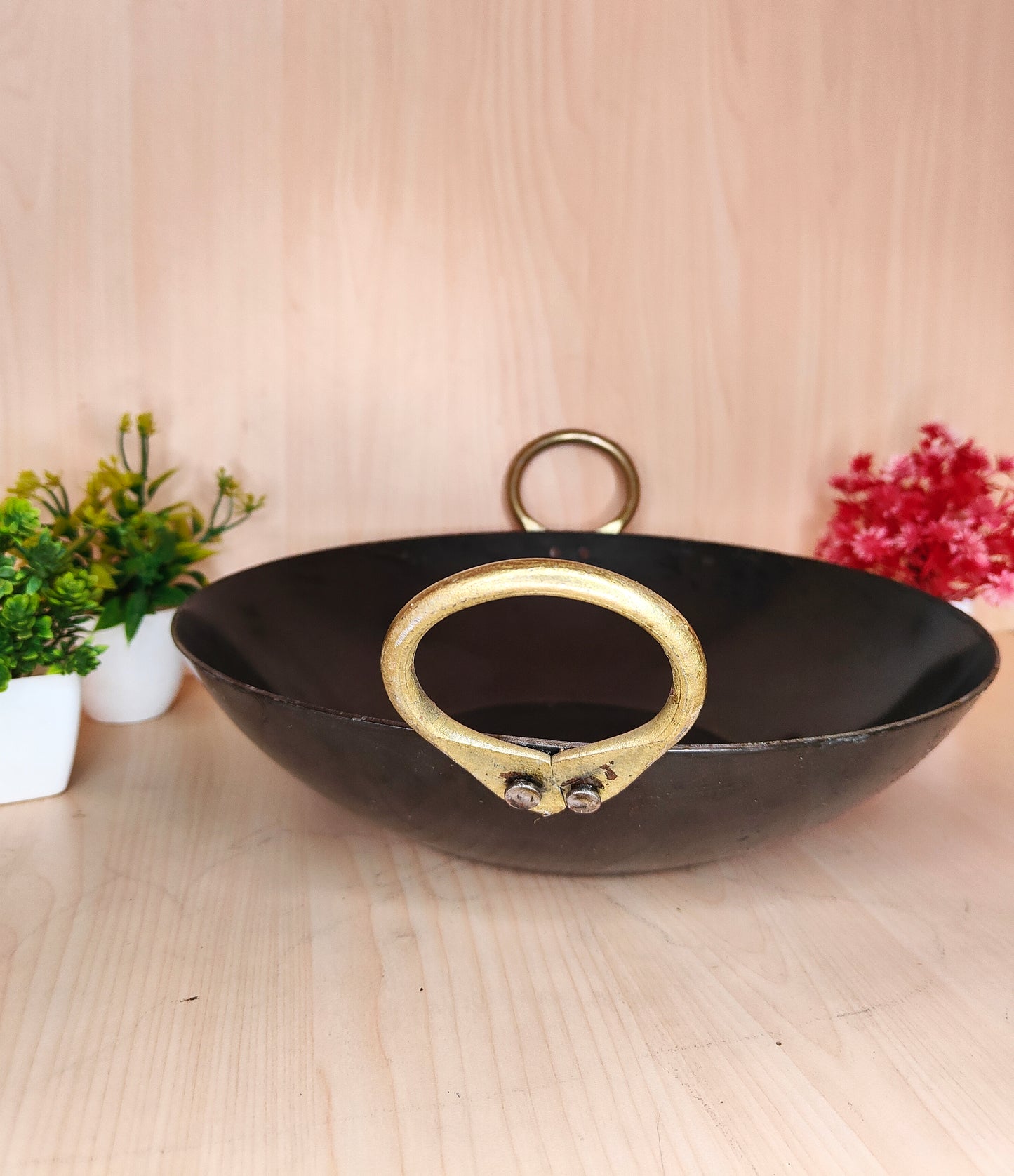 Black wok with gold handles on a light wooden surface