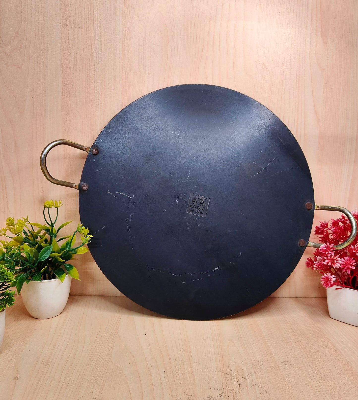 Black wok on a wooden surface with plants on either side