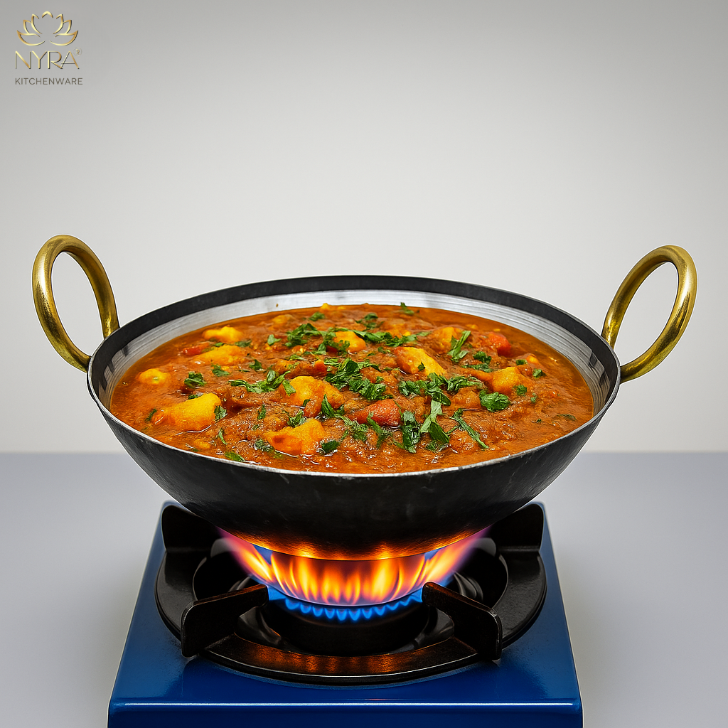Black wok with a colorful curry on a blue hot plate, featuring Nyra Kitchenware logo.