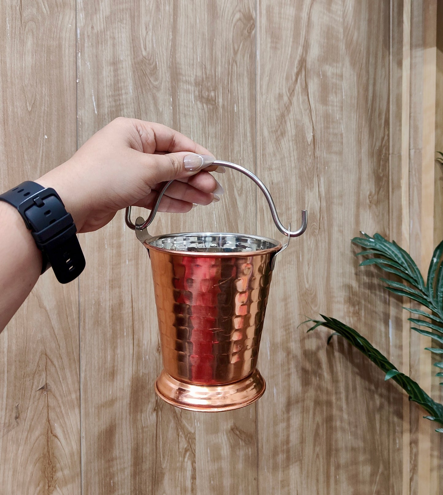 Copper bucket held by a hand against a wooden background