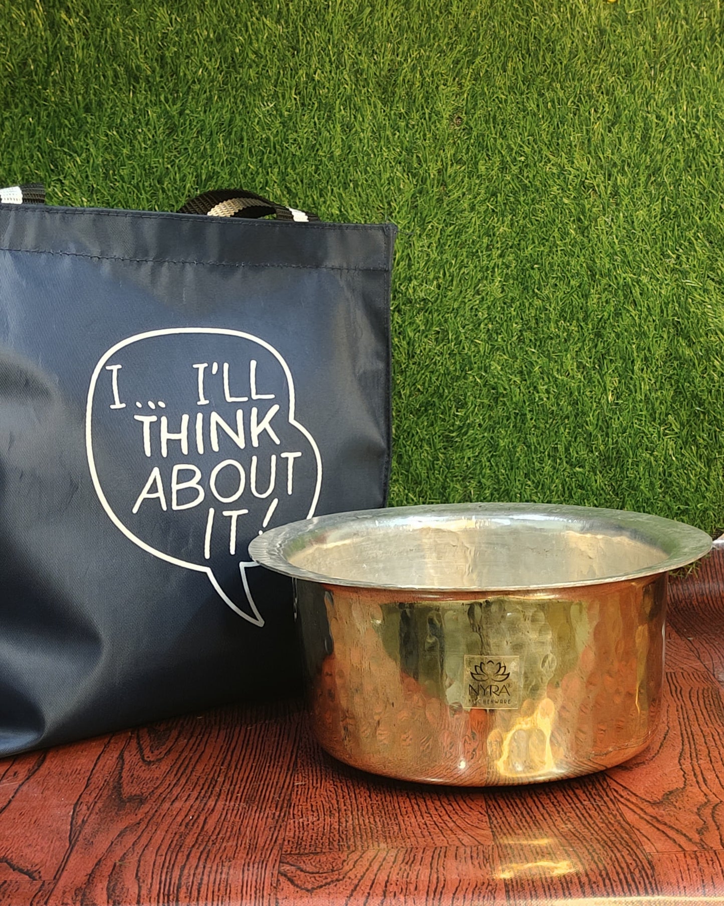 Copper pot on a wooden surface with a blue bag labeled 'I'll Think About It' in the background.