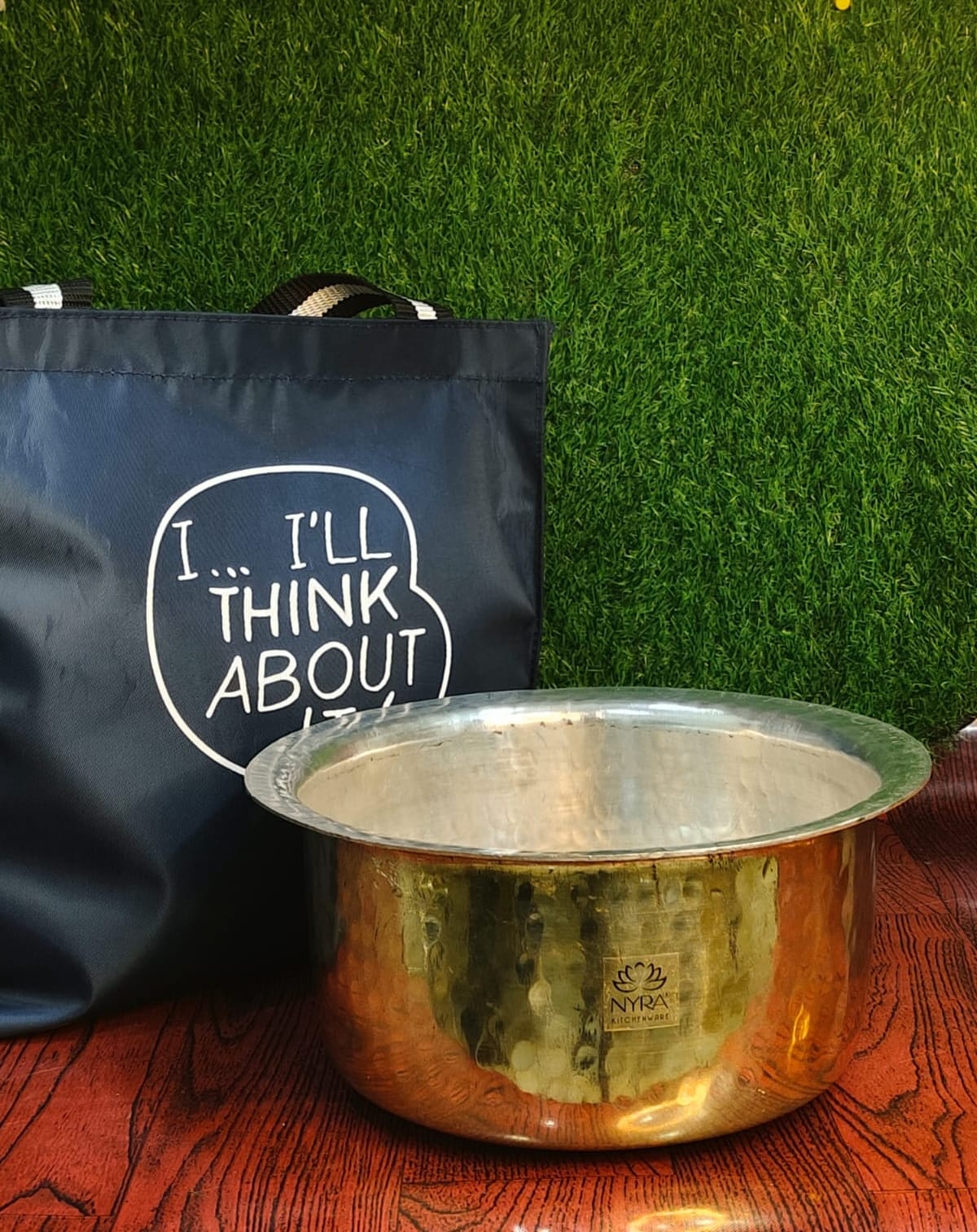 Gold pot and black bag with text on a wooden surface and green grass background