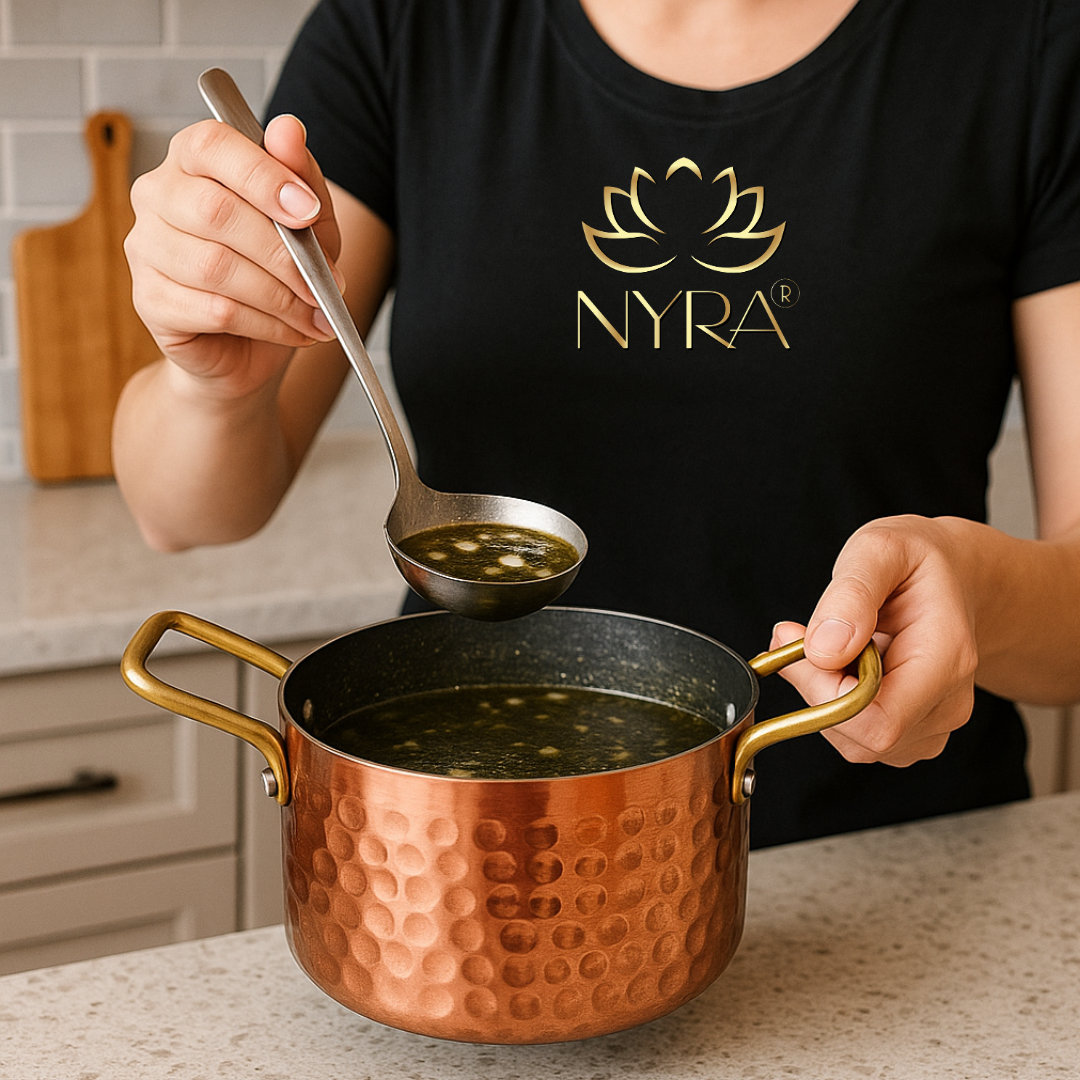 Person ladling soup from a copper pot into a spoon, wearing a black NYRA t-shirt.