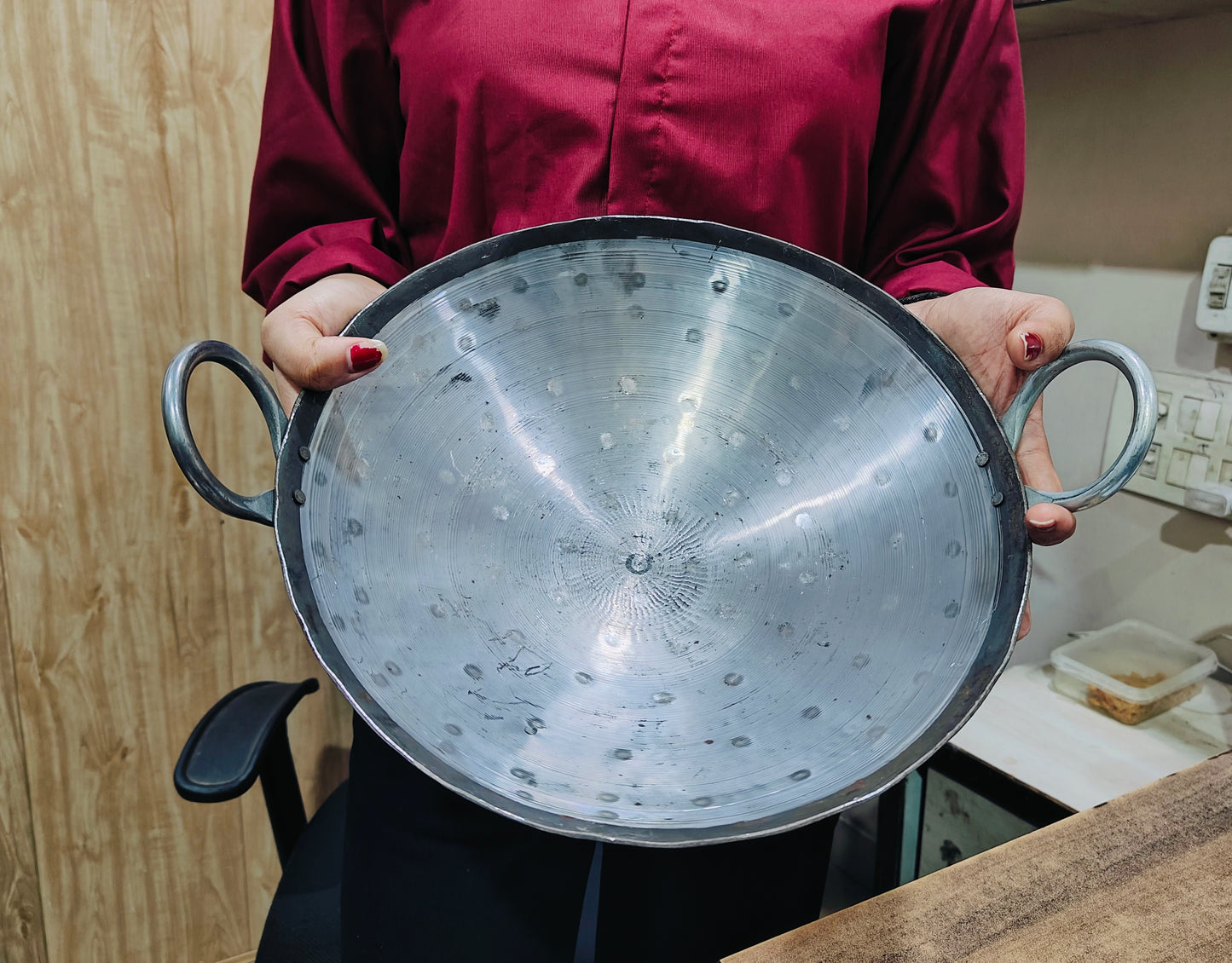 Person holding a large metal strainer in a kitchen setting