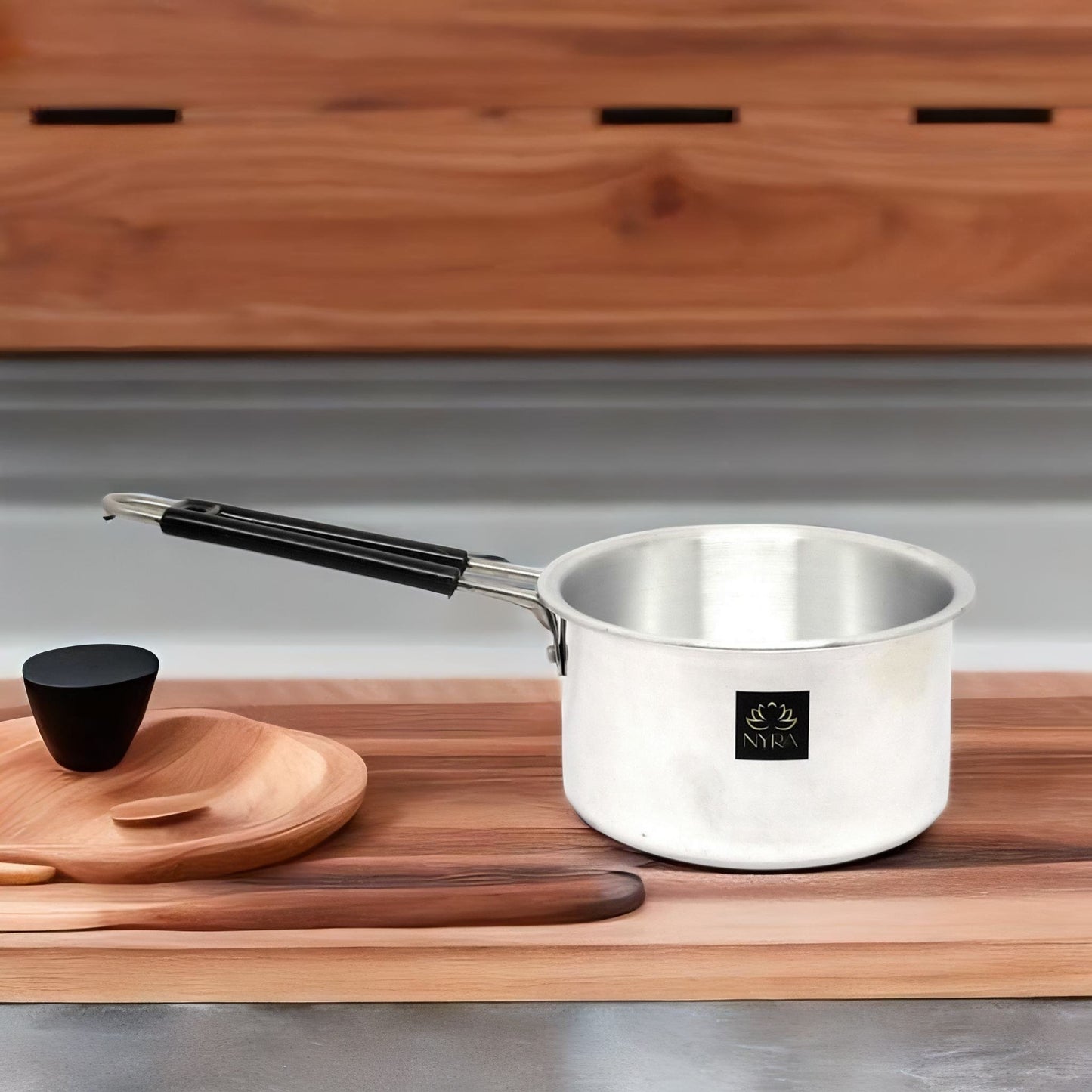 Silver pot with black handle on a wooden cutting board