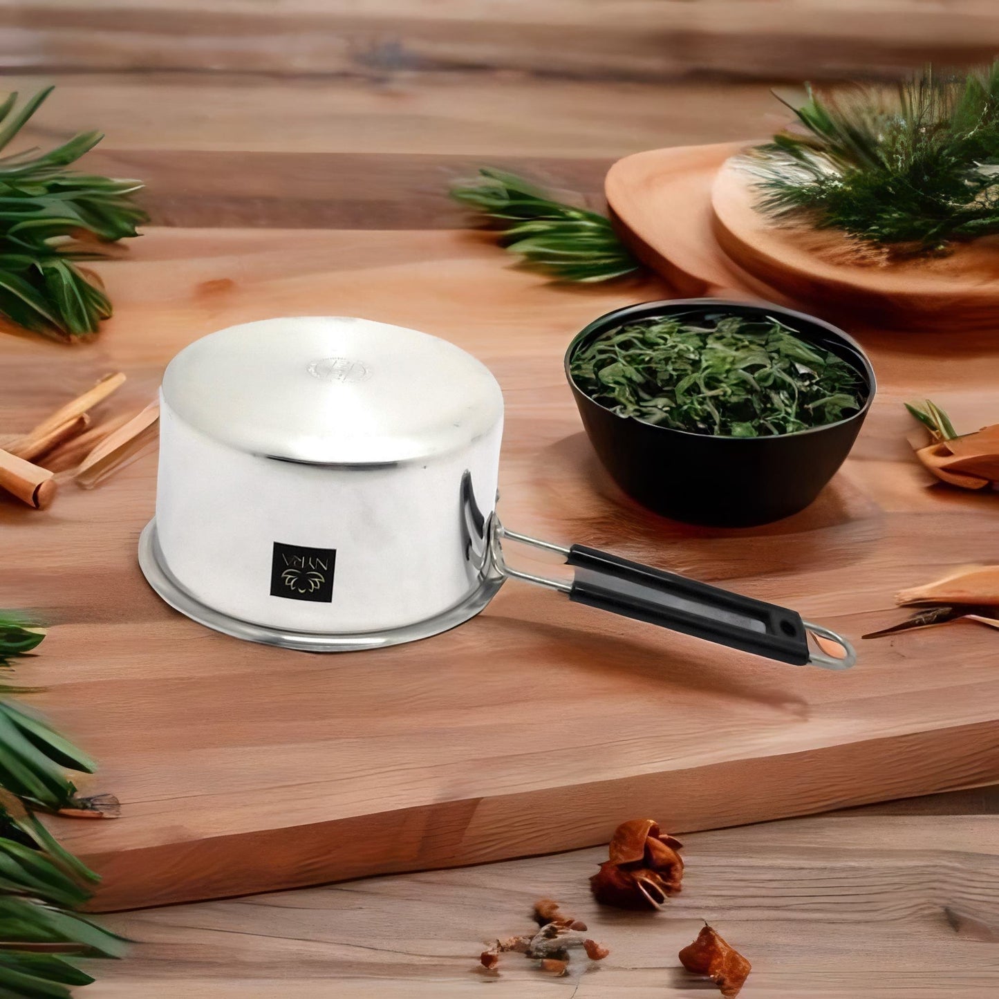 Small white pot with a black handle on a wooden surface with greenery and cinnamon sticks.