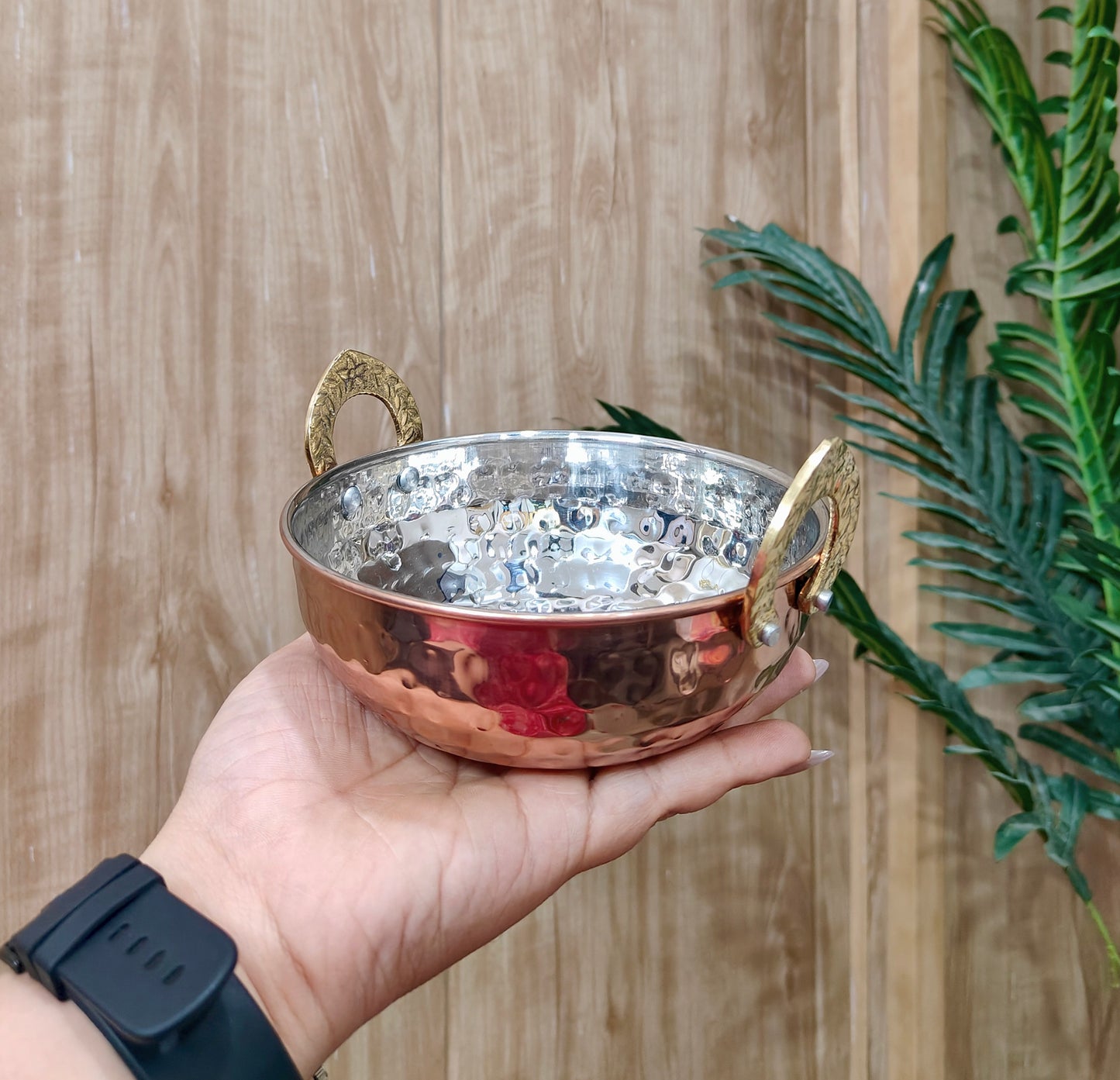 Copper bowl with handles held by a hand against a wooden background