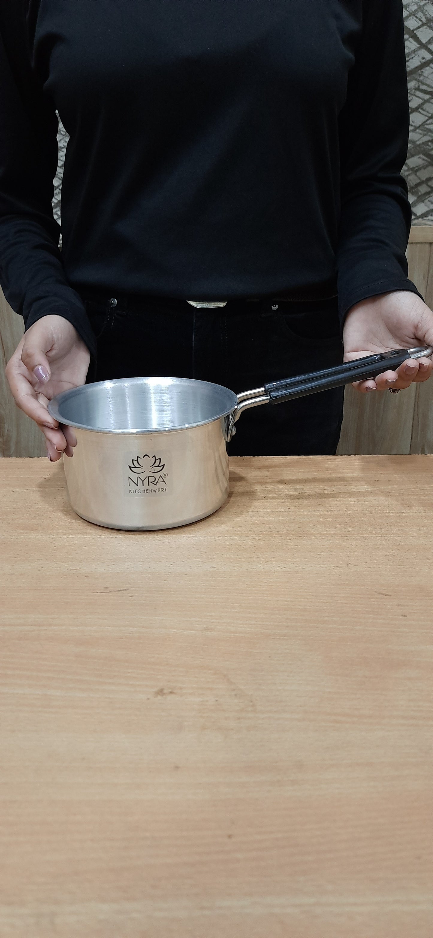 Person holding a metal spatula over a wooden surface with a visible brand logo.