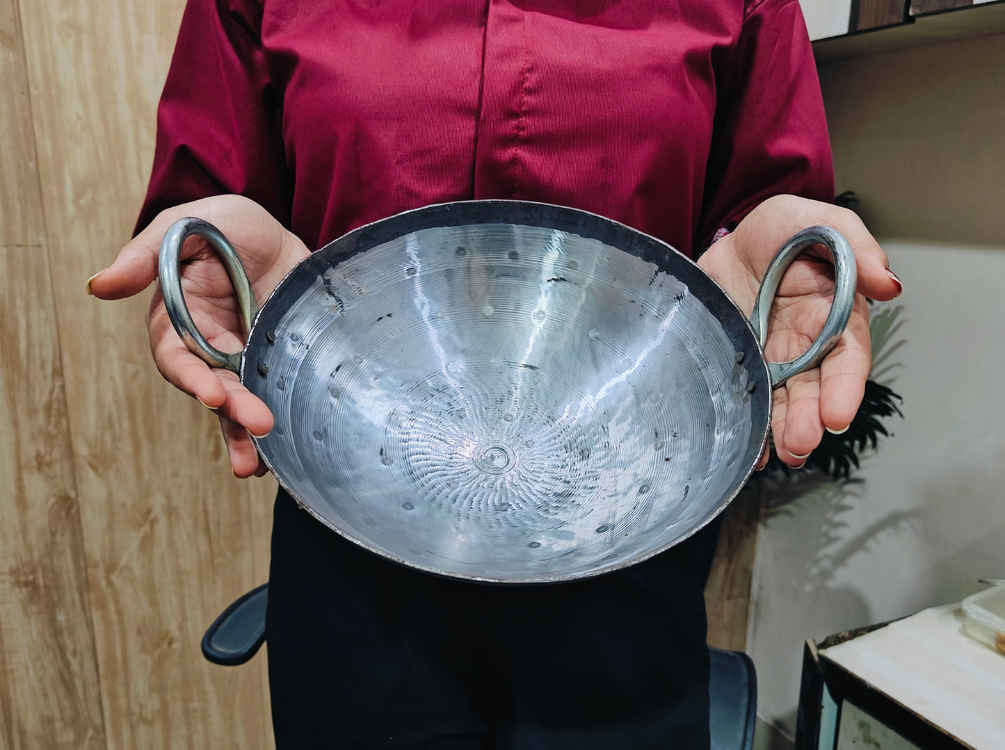 Person holding a metal bowl with handles against a neutral background