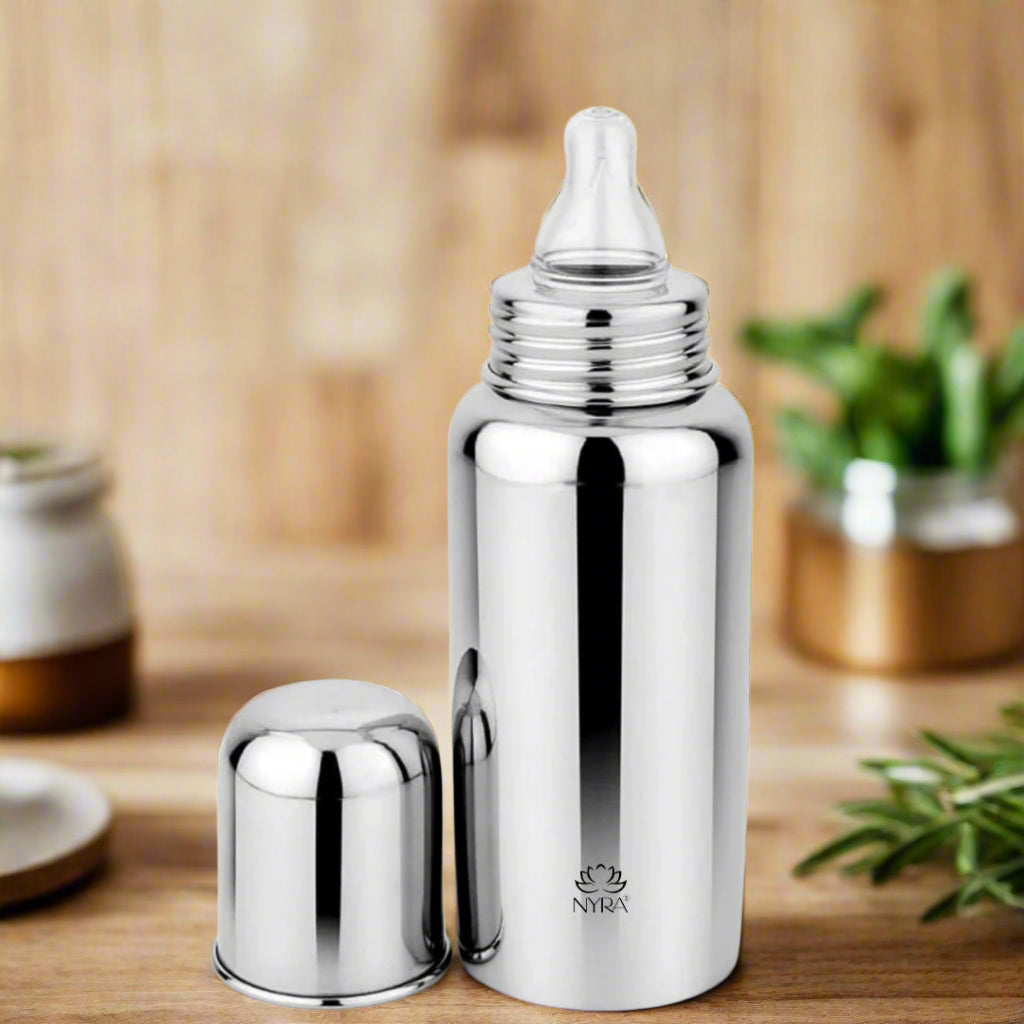 A stainless steel baby feeding bottle with a nipple, alongside its closed cap, presented on a wooden surface.