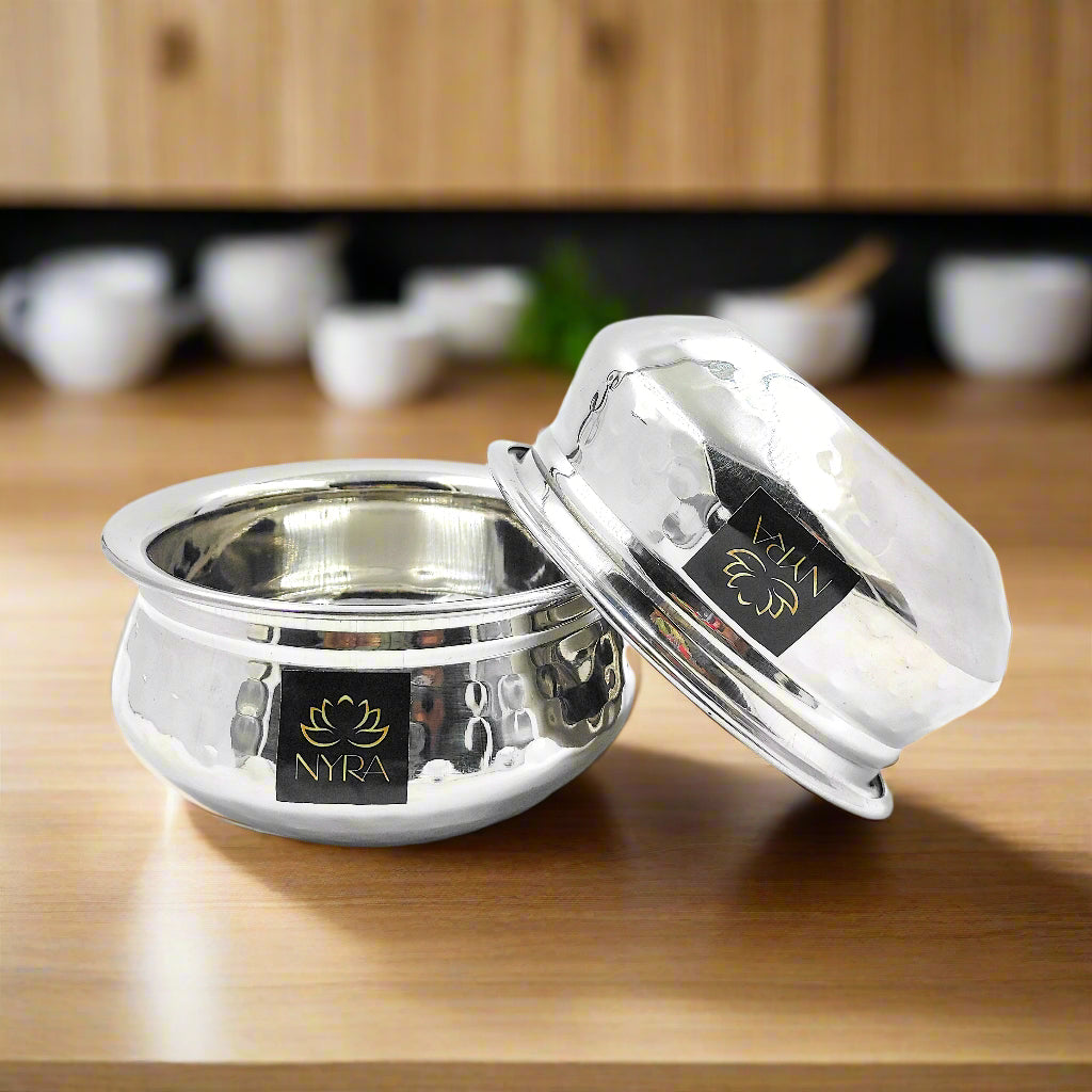 A stainless steel hammered finish dal handi, with a lid, placed on a wooden surface, reflecting light on its textured surface.