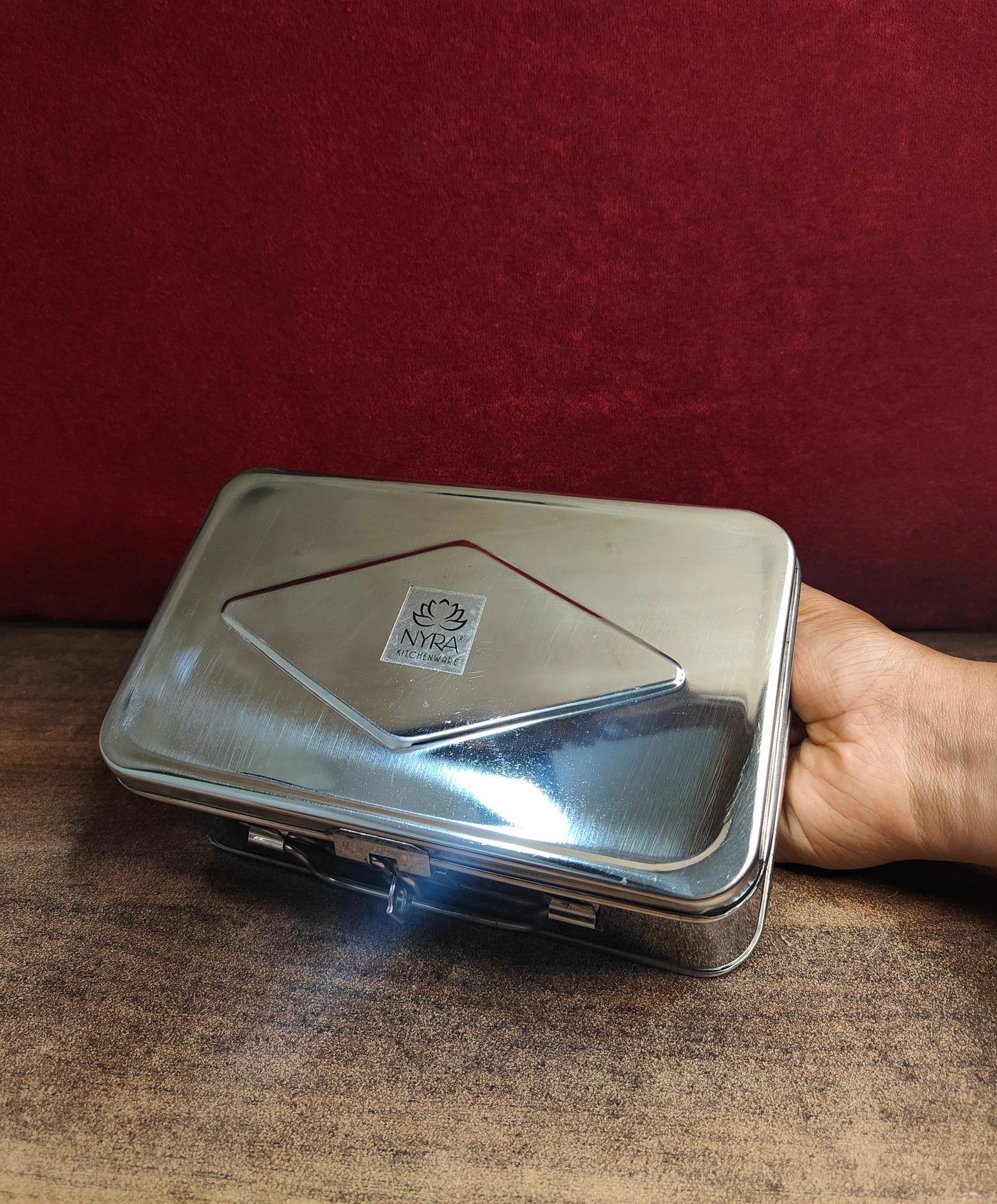 Metal cash box with a brand logo held by a hand against a red background