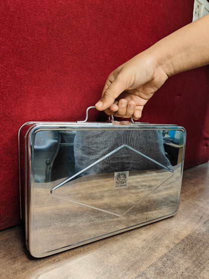 Metallic briefcase with a visible brand logo held by a hand against a red background
