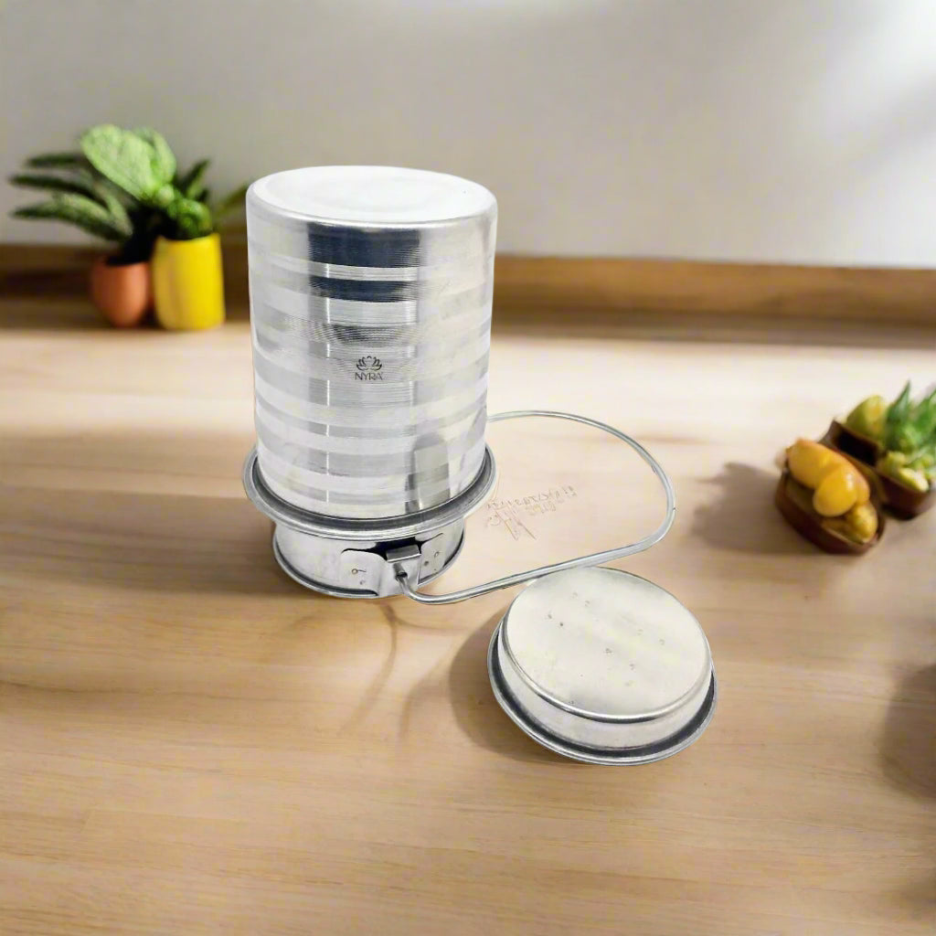 A stainless steel jointless milk can with a lid on a table, with a plant and fruits in the background.