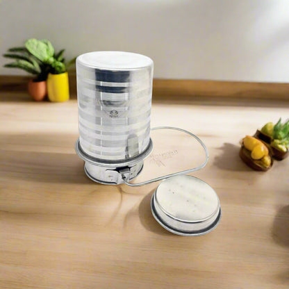 A stainless steel jointless milk can with a lid on a table, with a plant and fruits in the background.