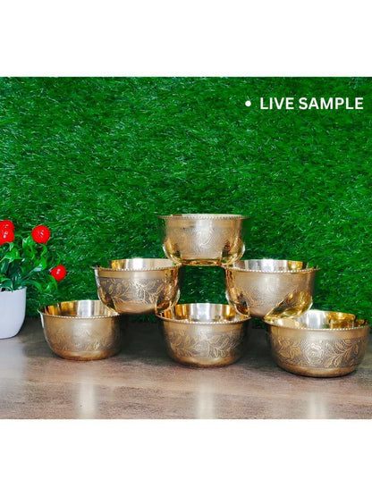 Five metallic gold bowls with engraved patterns, arranged on a wooden surface against a green artificial grass backdrop. A small potted plant with red flowers is visible on the left, and the text 'LIVE SAMPLE' appears in the top right corner.