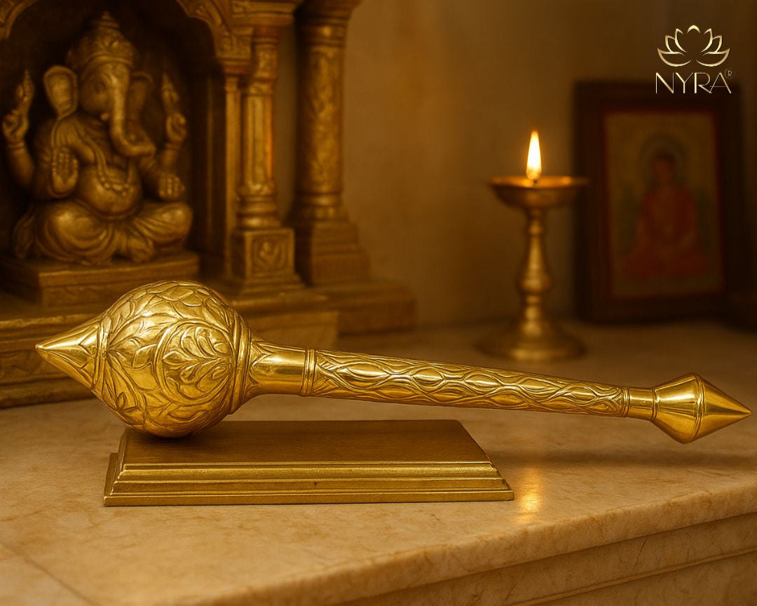 Decorative gada on a marble surface with a blurred background featuring a statue and candle.