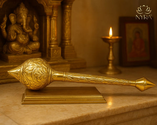 Decorative gada on a marble surface with a blurred background featuring a statue and candle.