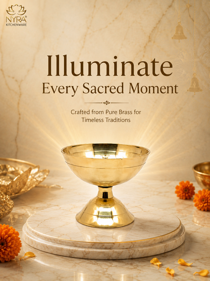 A polished brass pedestal bowl, also known as a kalash, displayed on a marble slab. The background is a warm beige marble wall with golden light rays emanating from the bowl.