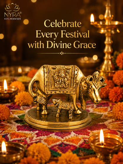 A brass cow and calf idol displayed on a decorated festive surface with lit oil lamps and marigold flowers. The image includes the NYRA KITCHENWARE logo and the text 'Celebrate Every Festival with Divine Grace'.