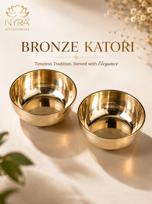 Two polished bronze katori serving bowls on a warm cream background with decorative dried flowers and green leaves. The NYRA Kitchenware logo and the text 'BRONZE KATORI' are displayed at the top.