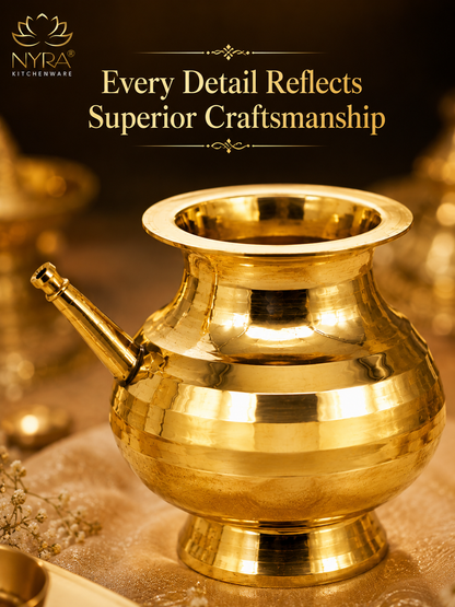 A polished brass traditional Indian pitcher or samovar with a spout, shown on a warm golden surface with decorative elements and the NYRA Kitchenware logo and text at the top.