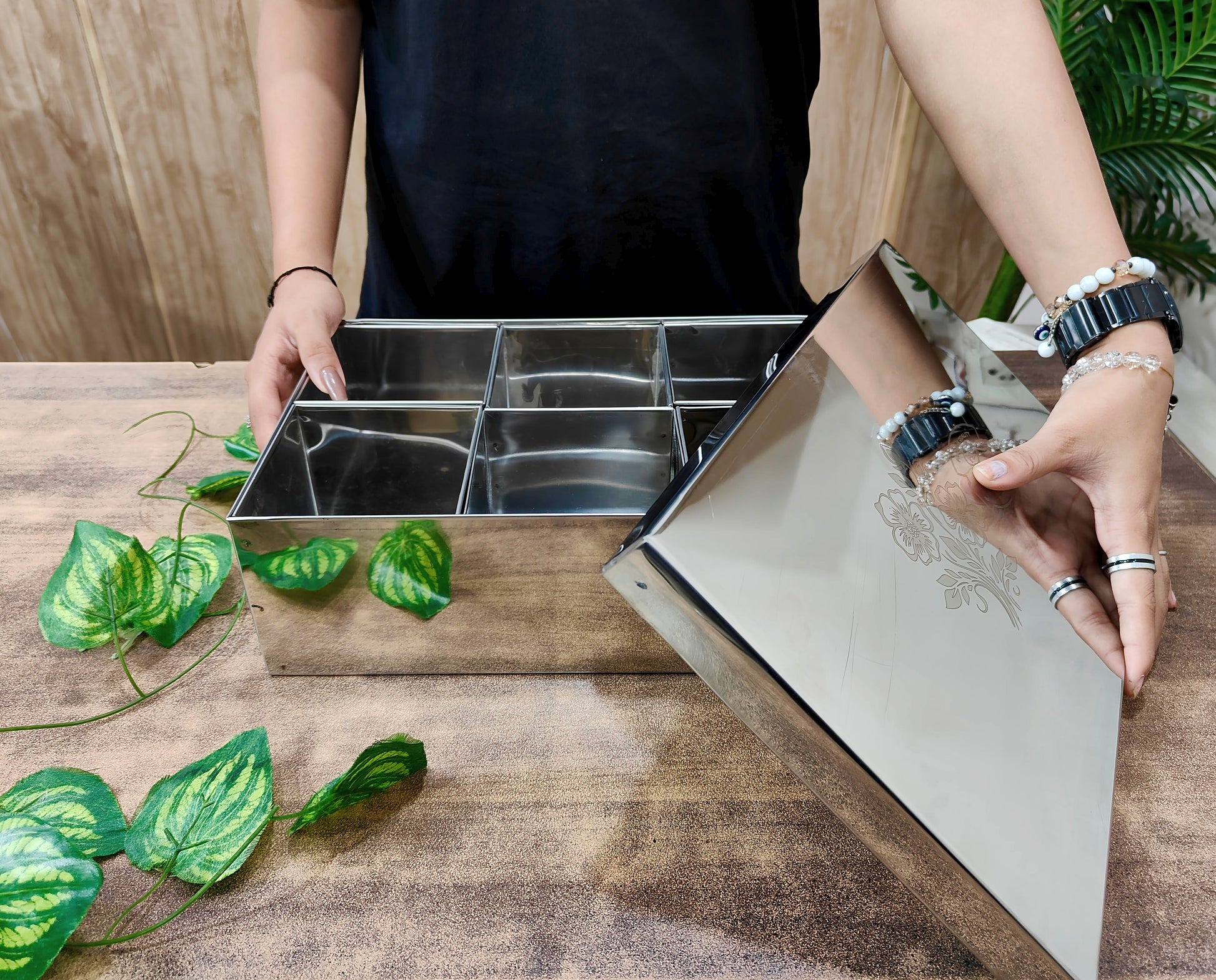 Person opening a stainless steel kitchen drawer with compartments on a wooden surface.