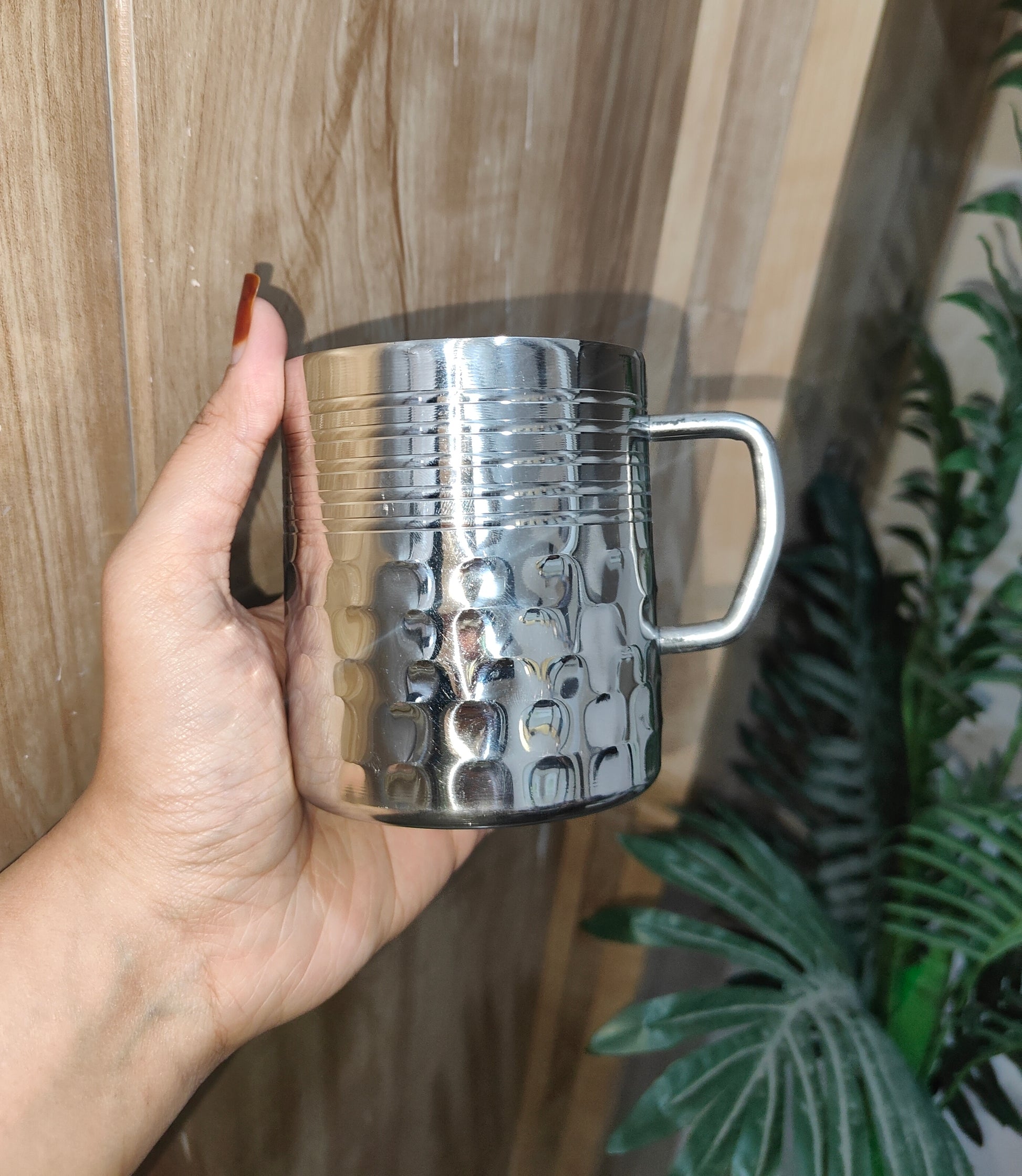 Hand holding a silver textured mug against a wooden background