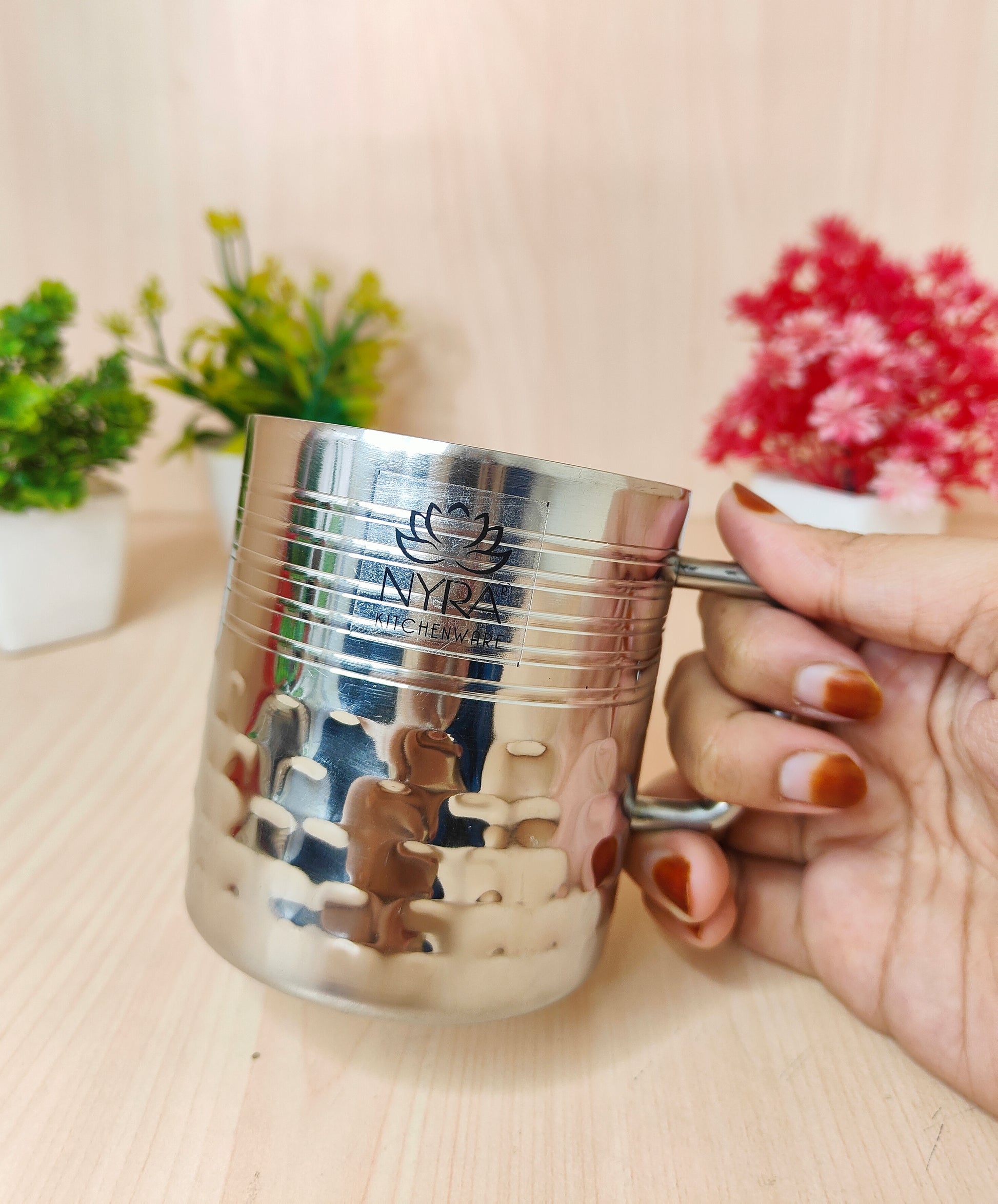 Silver cup with a logo held by a hand on a light surface with plants in the background