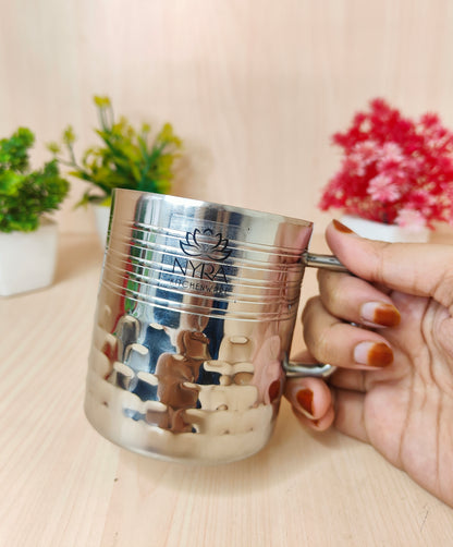 Silver cup with a logo held by a hand on a light surface with plants in the background