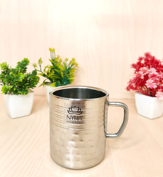 Silver metal mug with a logo on a light surface with plants in the background