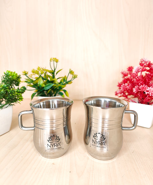 Two silver pitchers with 'Nyra' branding on a light surface with plants in the background.