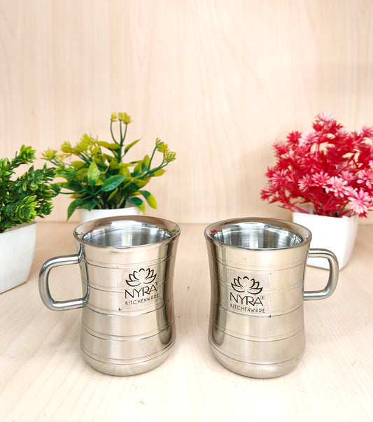 Two silver mugs with 'Nyra Kitchenware' logo on a light surface with plants in the background.