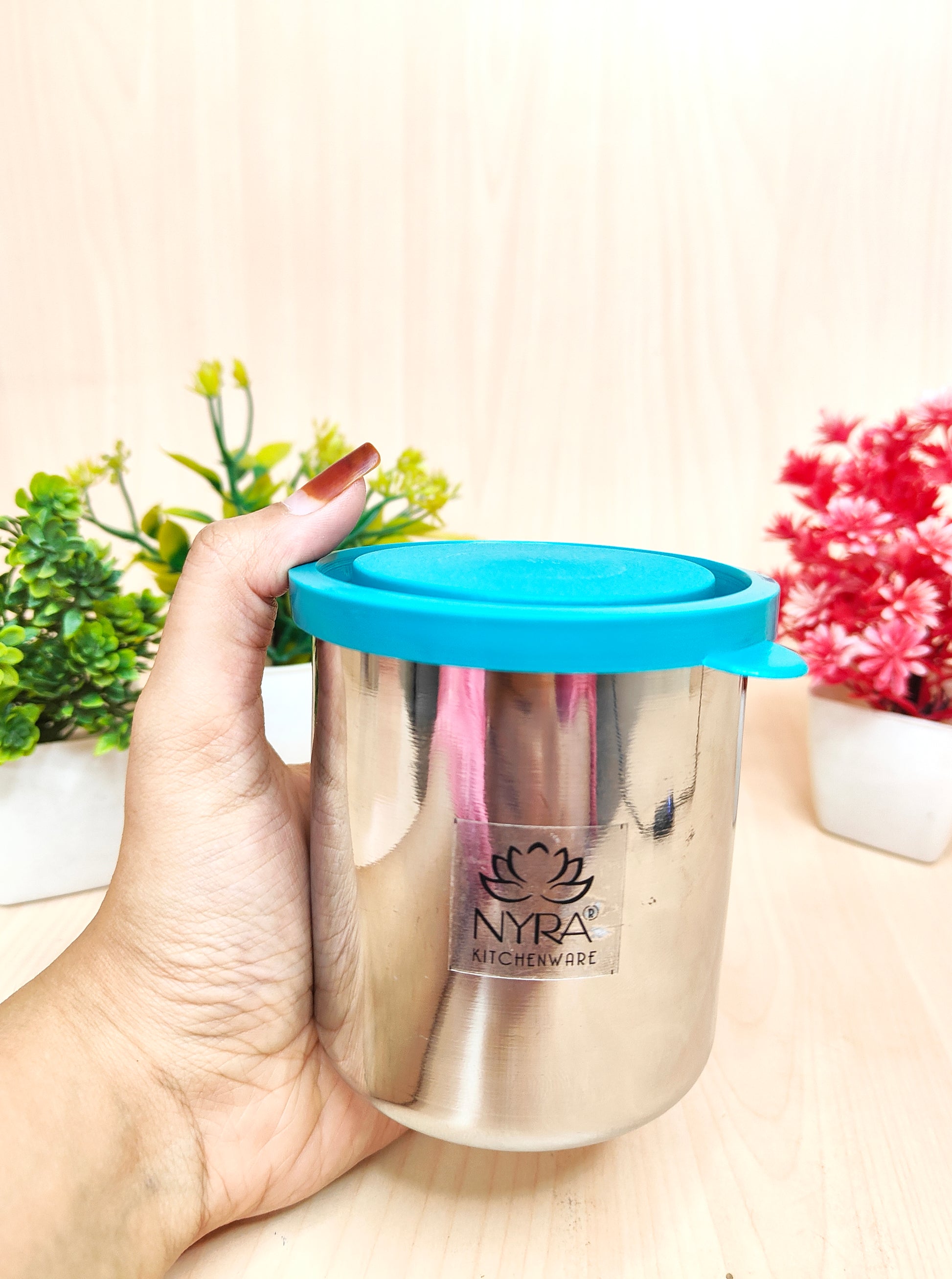 Stainless steel container with blue lid held by a hand on a light background