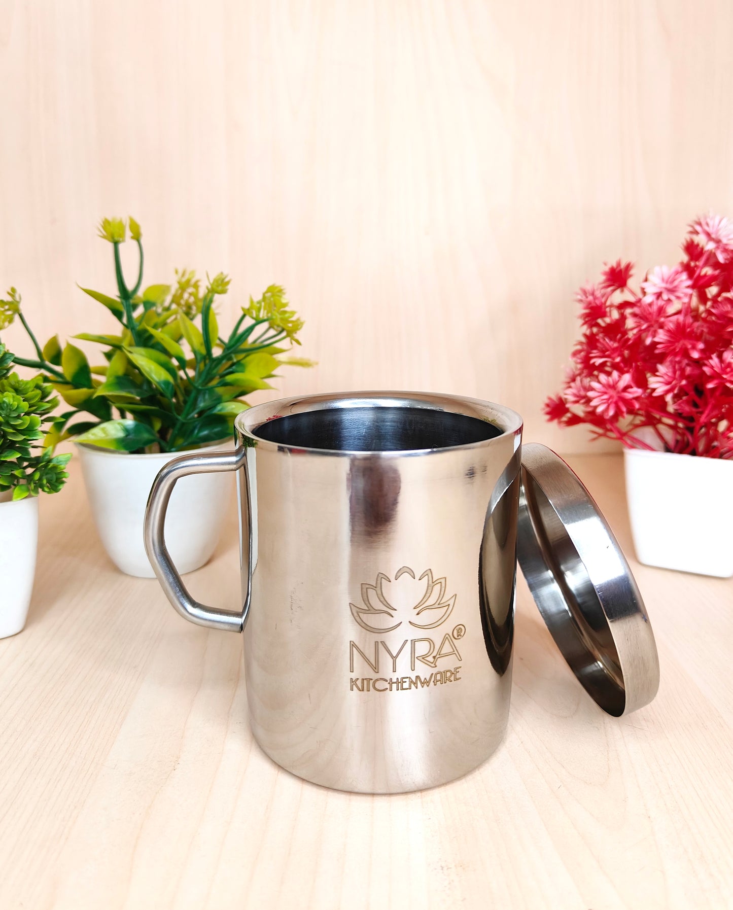 Stainless steel mug with handle and lid on a light surface with plants in the background