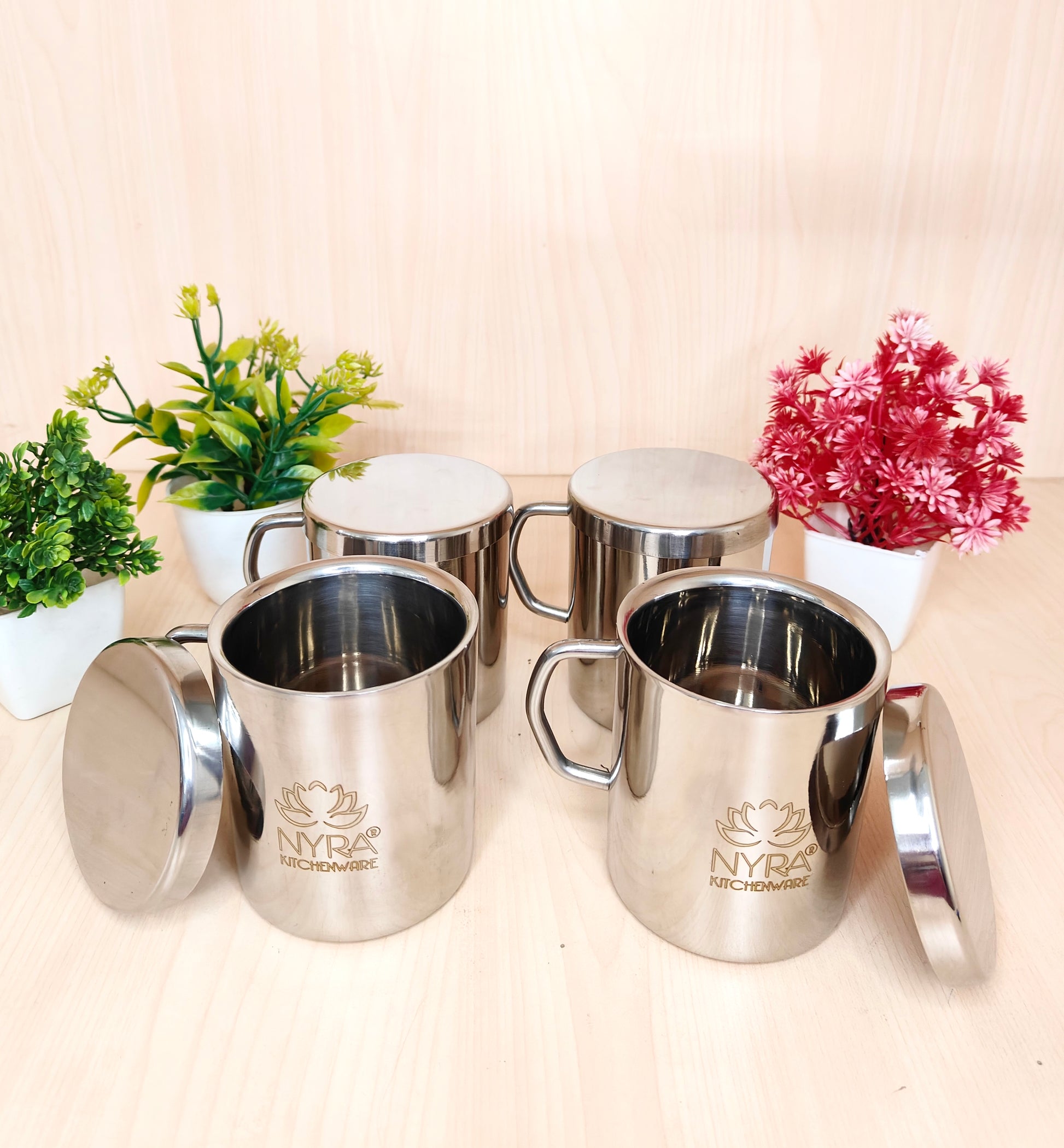 Set of silver mugs with lids on a light background, featuring the Nyra Kitchenware logo.