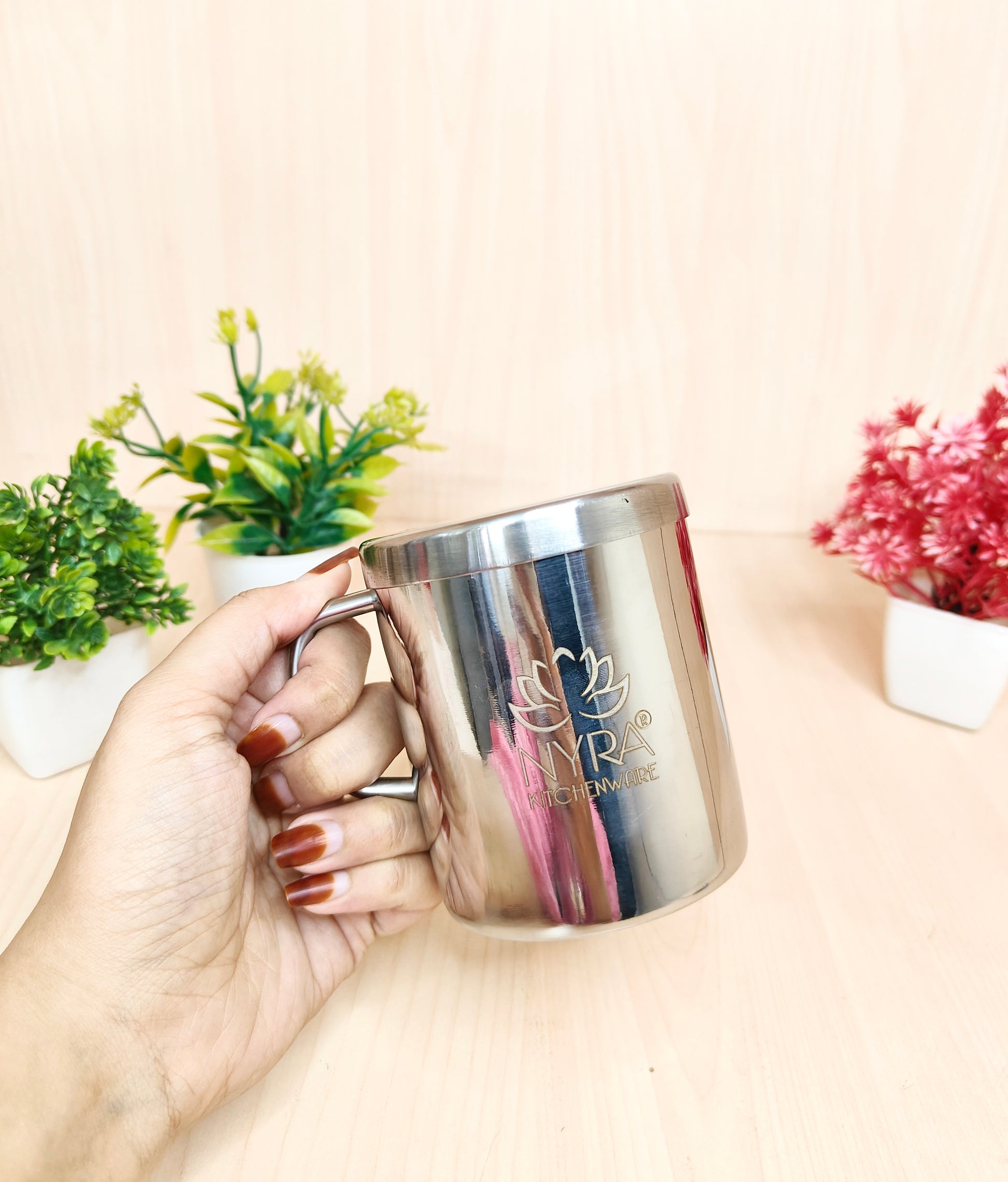 Hand holding a silver mug with a logo on a light background
