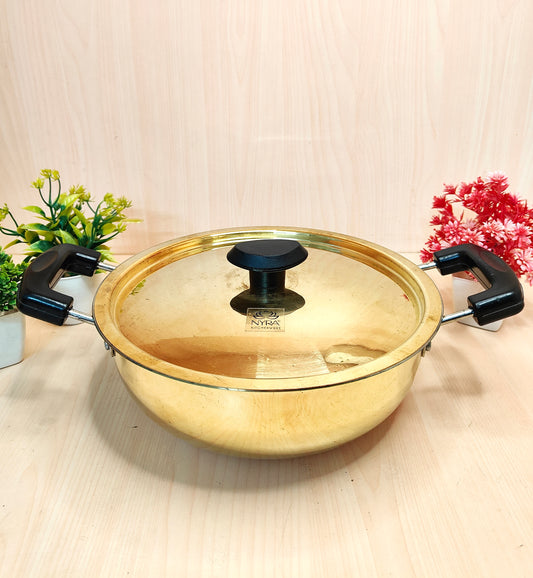 Gold-colored pot with a lid on a light wooden surface with decorative plants.