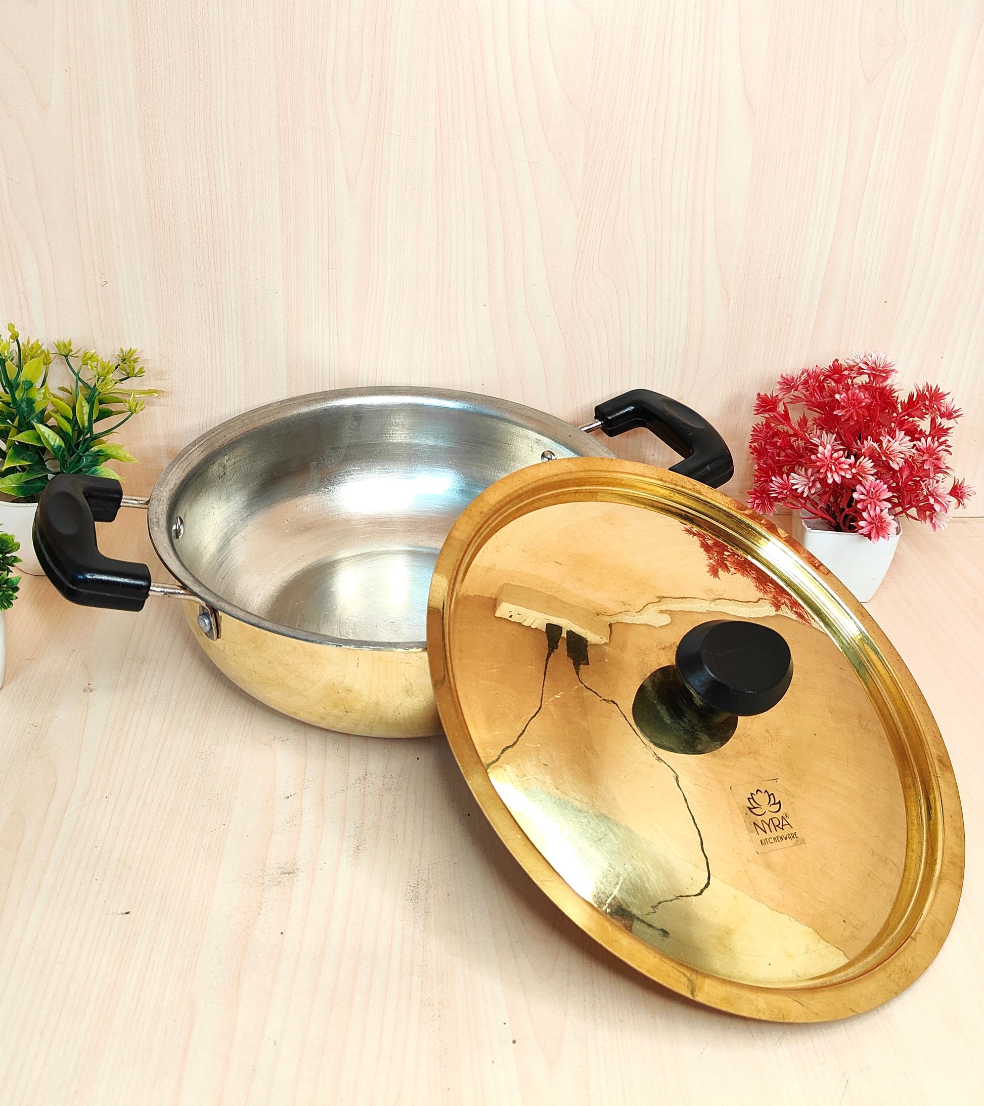 Stainless steel pot with a gold lid on a light wooden surface.