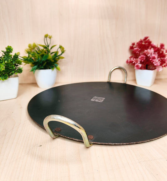 Black round tray with brass handles on a wooden surface with plants in the background