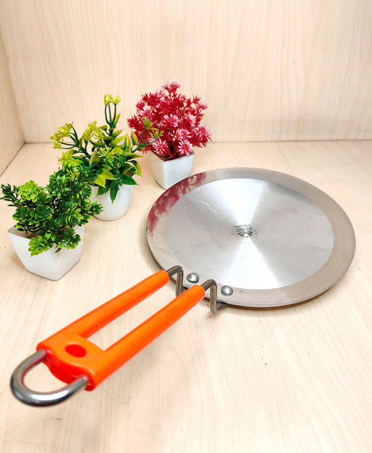 Metal camping pan with orange handle on a light wooden surface with plants in the background