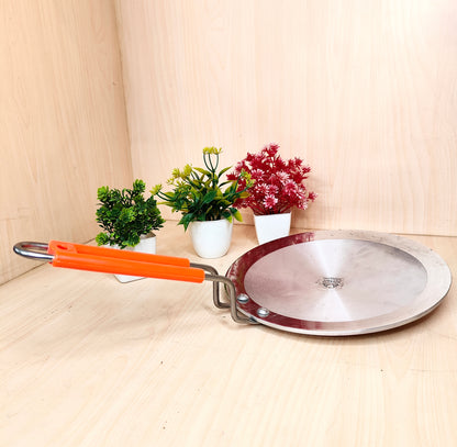 Metal frying pan with orange handle on a wooden surface with plants in the background